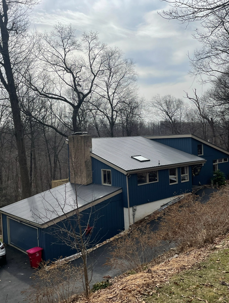 Blue house on a hill with a dark roof, surrounded by bare trees and a cloudy sky.