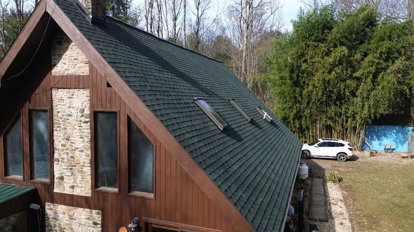 A house with a green roof, wooden siding, stone accents, and a white car parked outside.