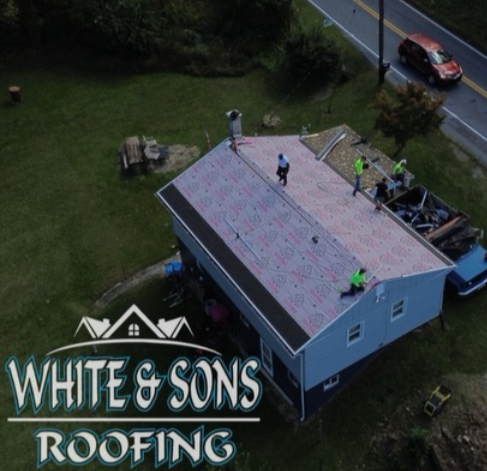 Roofing crew working on a blue house with green grass.  White & Sons Roofing logo displayed.