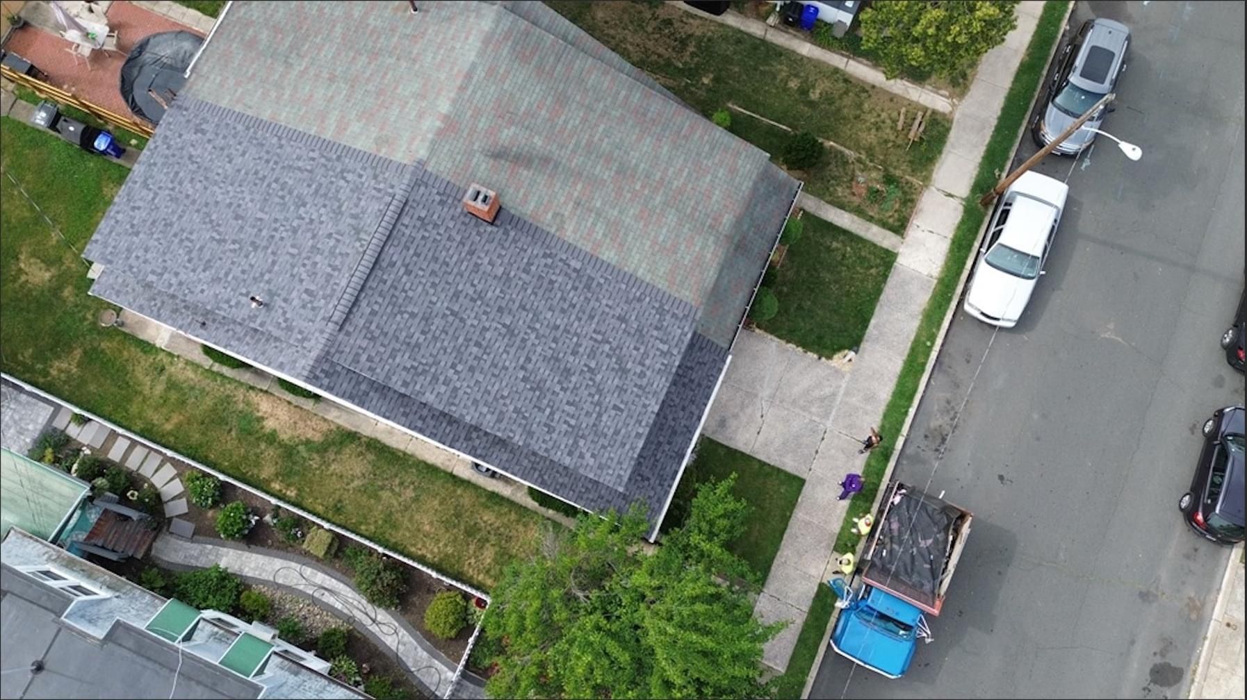 Overhead view of a house with a gray roof, cars parked on the street, and a blue truck.