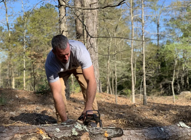 Man using a chainsaw to cut a log in a wooded area.