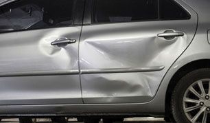 Silver sedan with a large dent on the rear passenger door and side panel