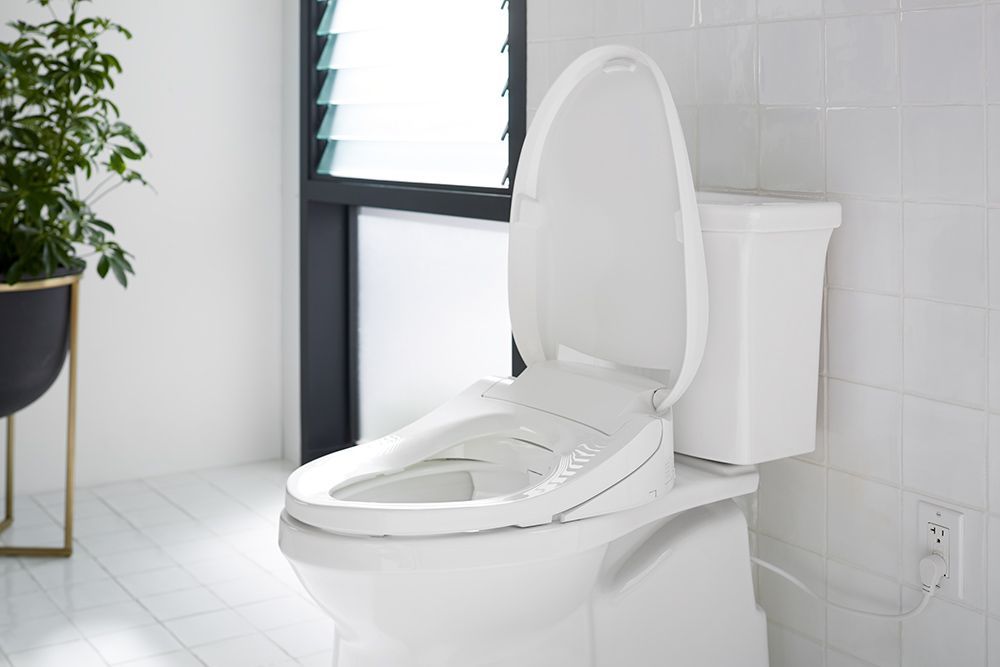 A white toilet is sitting in a bathroom next to a window.