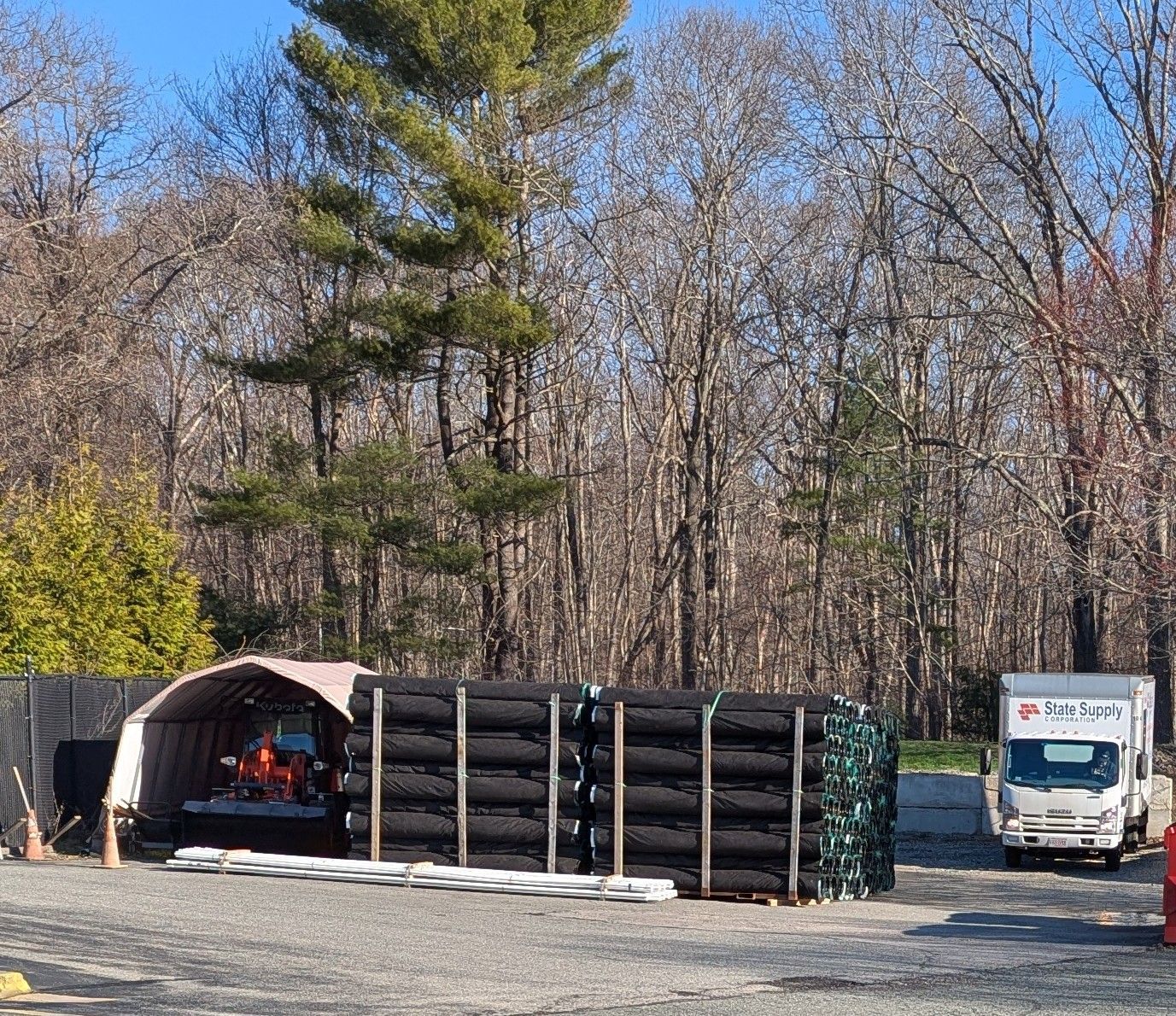 Tires stacked outdoors next to a work truck and equipment, set in a wooded area.