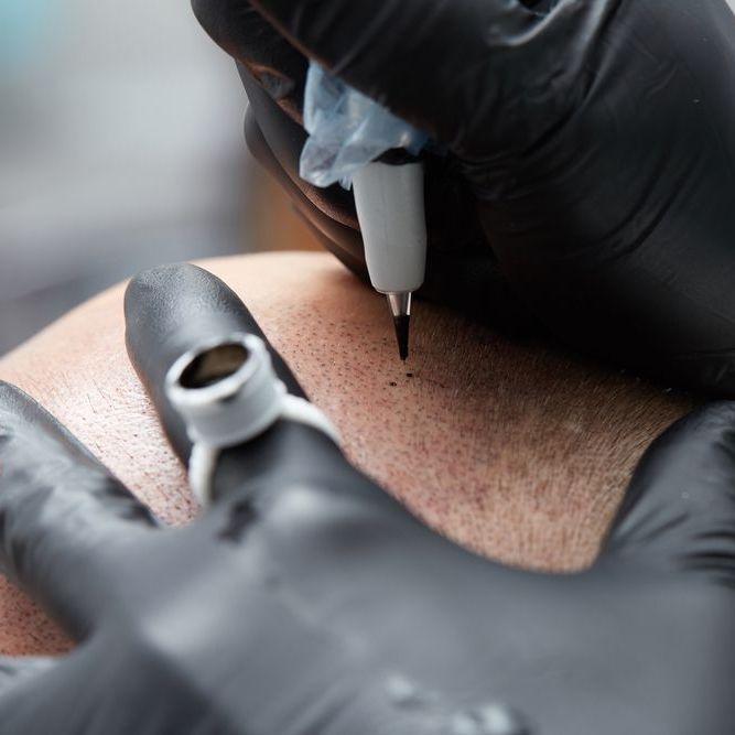 A person wearing black gloves is getting a tattoo on their arm.