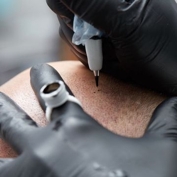 A person wearing black gloves is getting a tattoo on their arm.