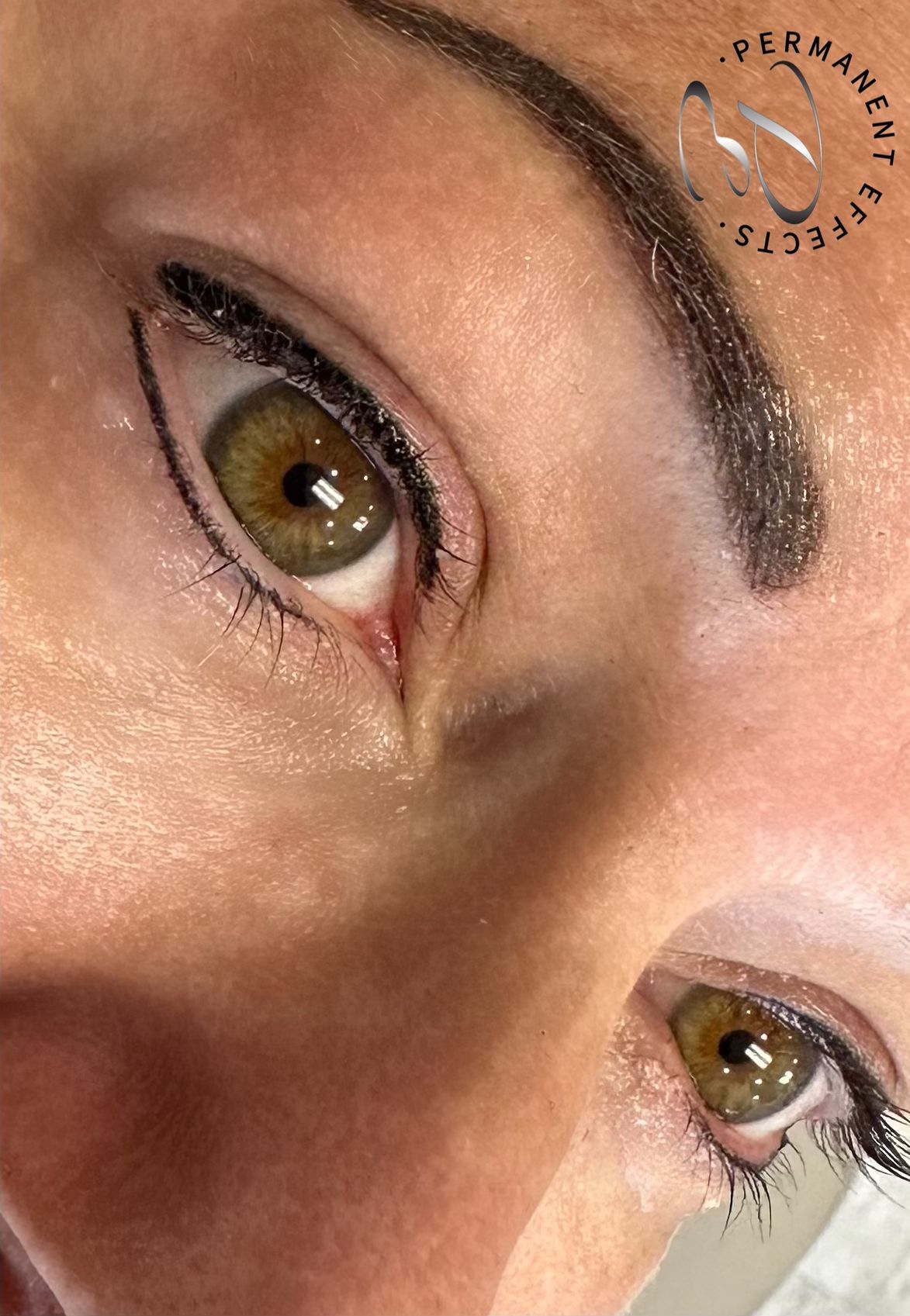 Close-up of a person's eye with permanent eyeliner and a filled-in eyebrow; the eye is green.