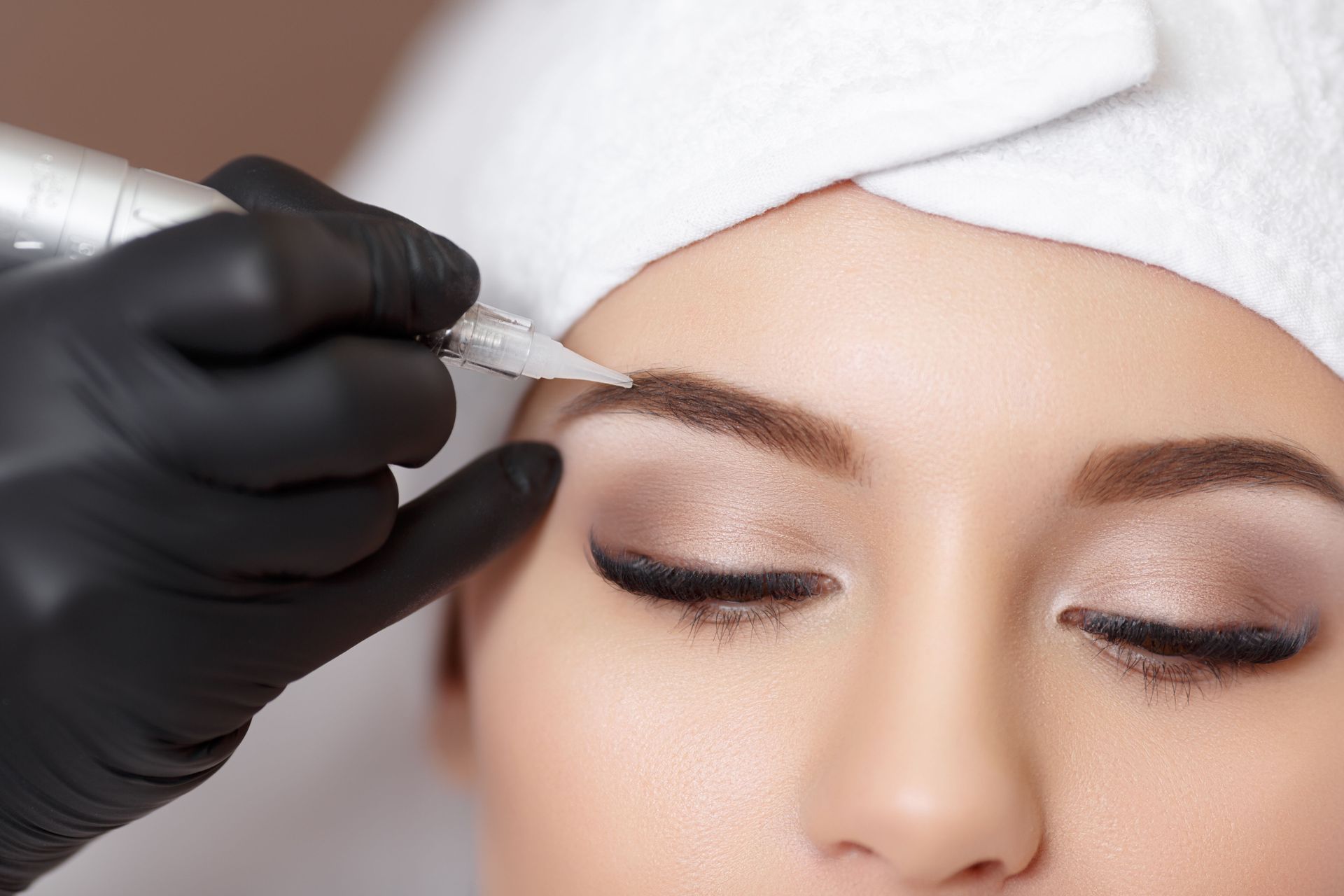 A woman is getting a permanent makeup tattoo on her eyebrows.