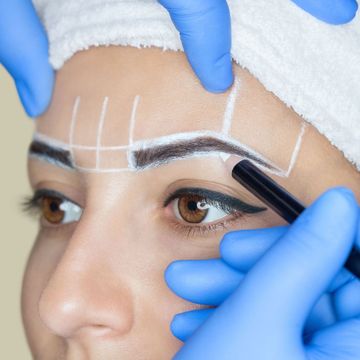 A woman is getting her eyebrows drawn by a makeup artist.