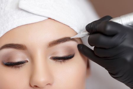 A woman is getting a permanent makeup tattoo on her eyebrows.