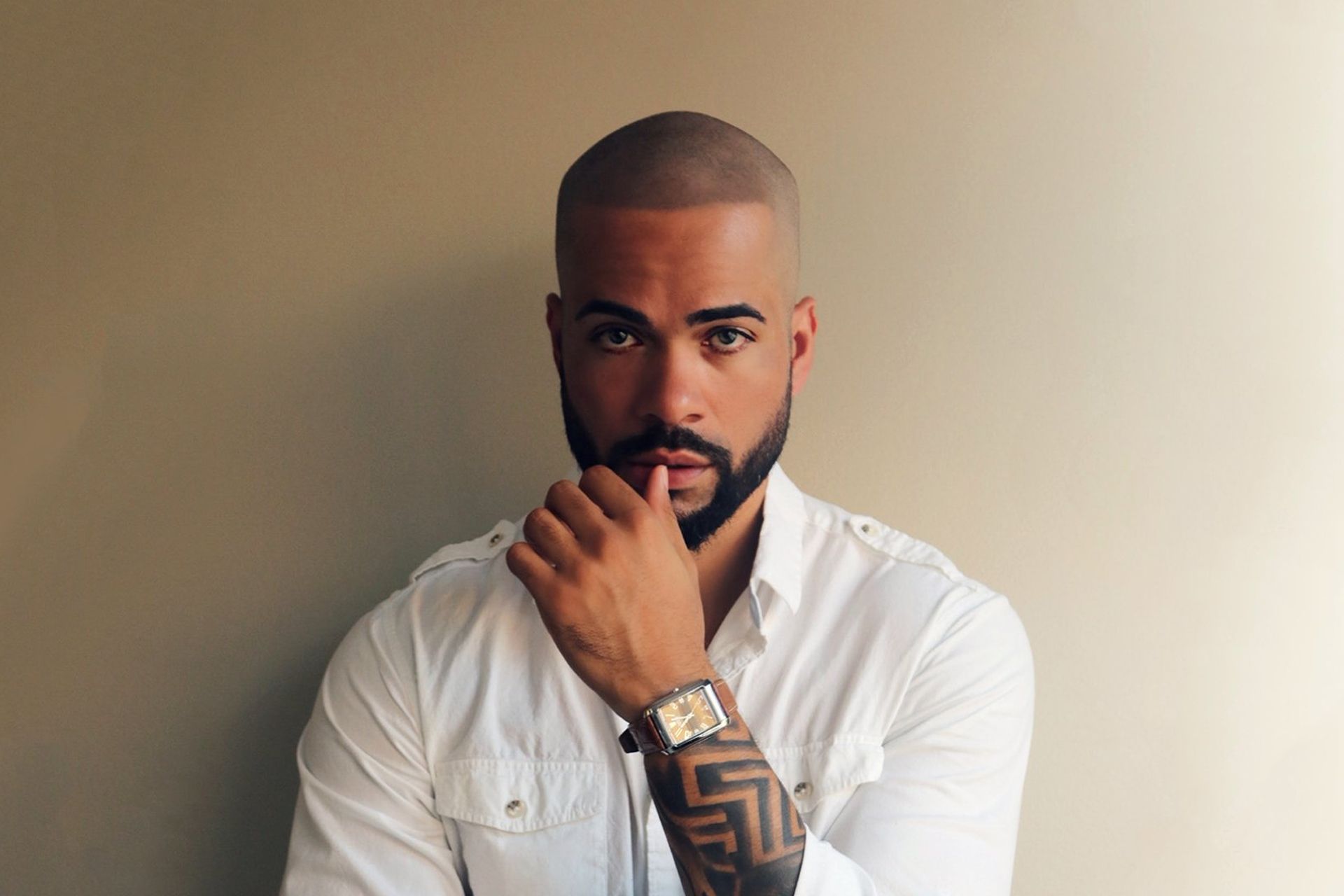 A man with a beard is wearing a white shirt and a watch.