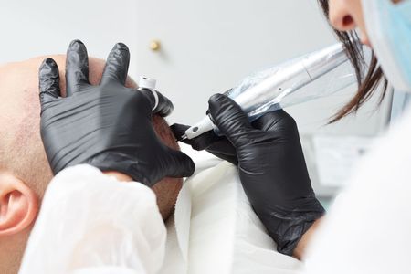 A woman is applying a tattoo to a man 's head.
