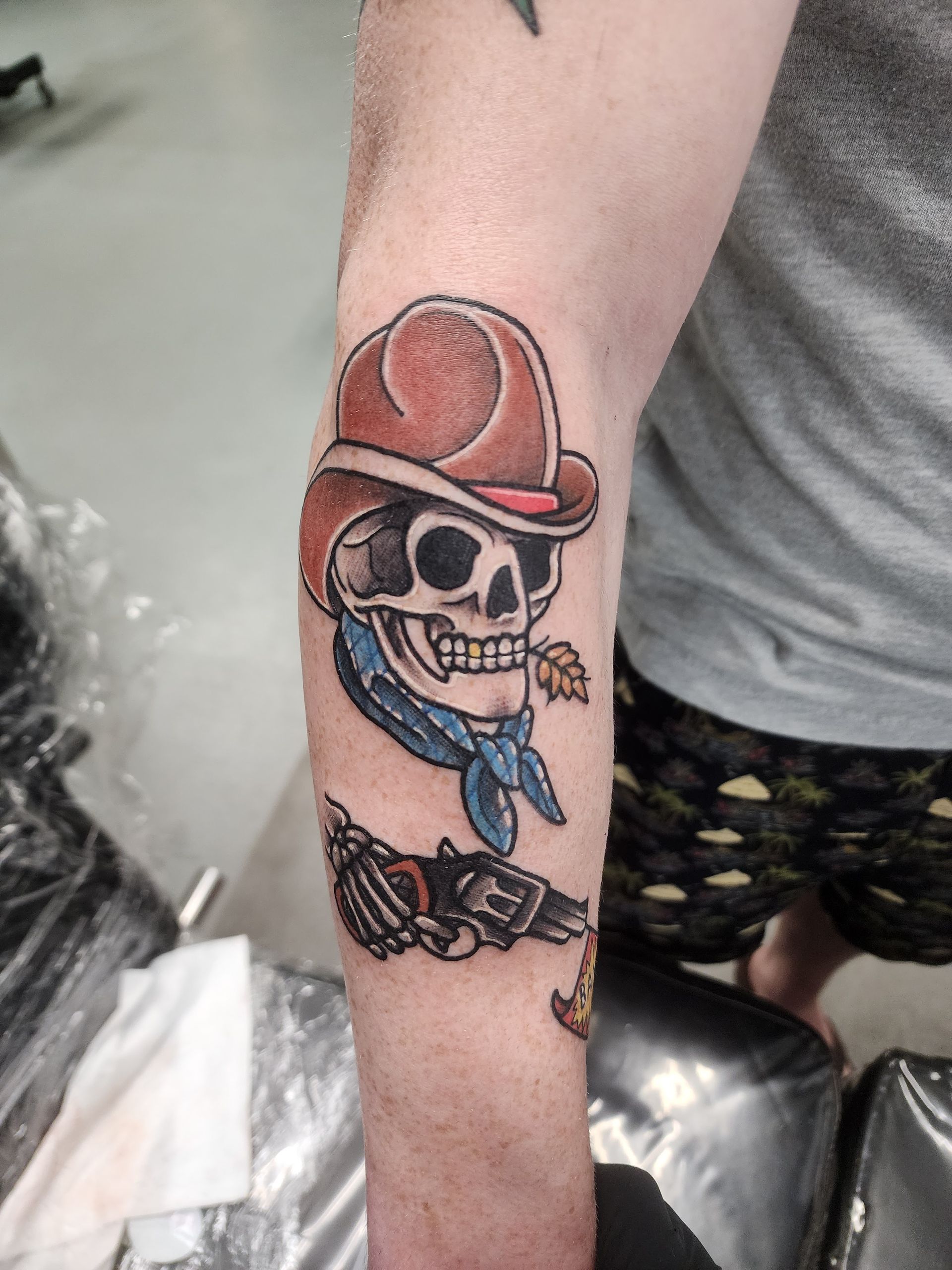 Tattoo of a skull wearing a cowboy hat and bandana. Below is a revolver.