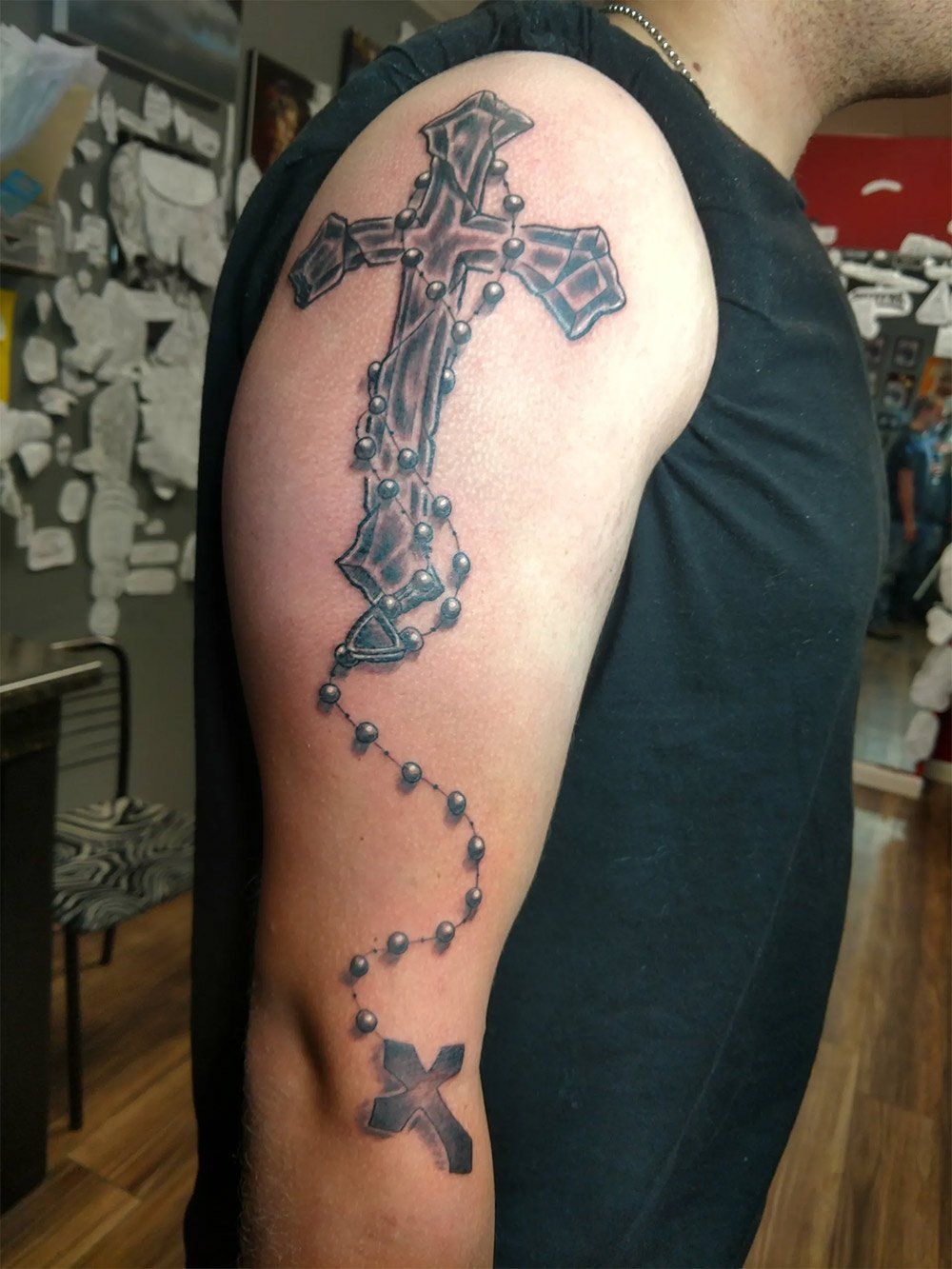 A man has a tattoo of a cross and rosary on his arm