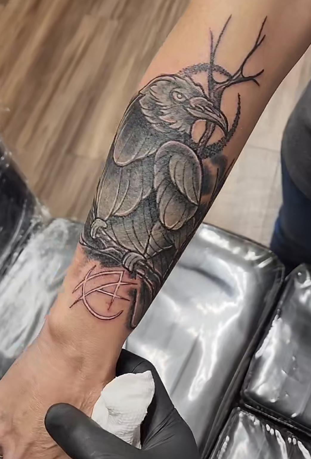 A person has a tattoo of a crow on their forearm