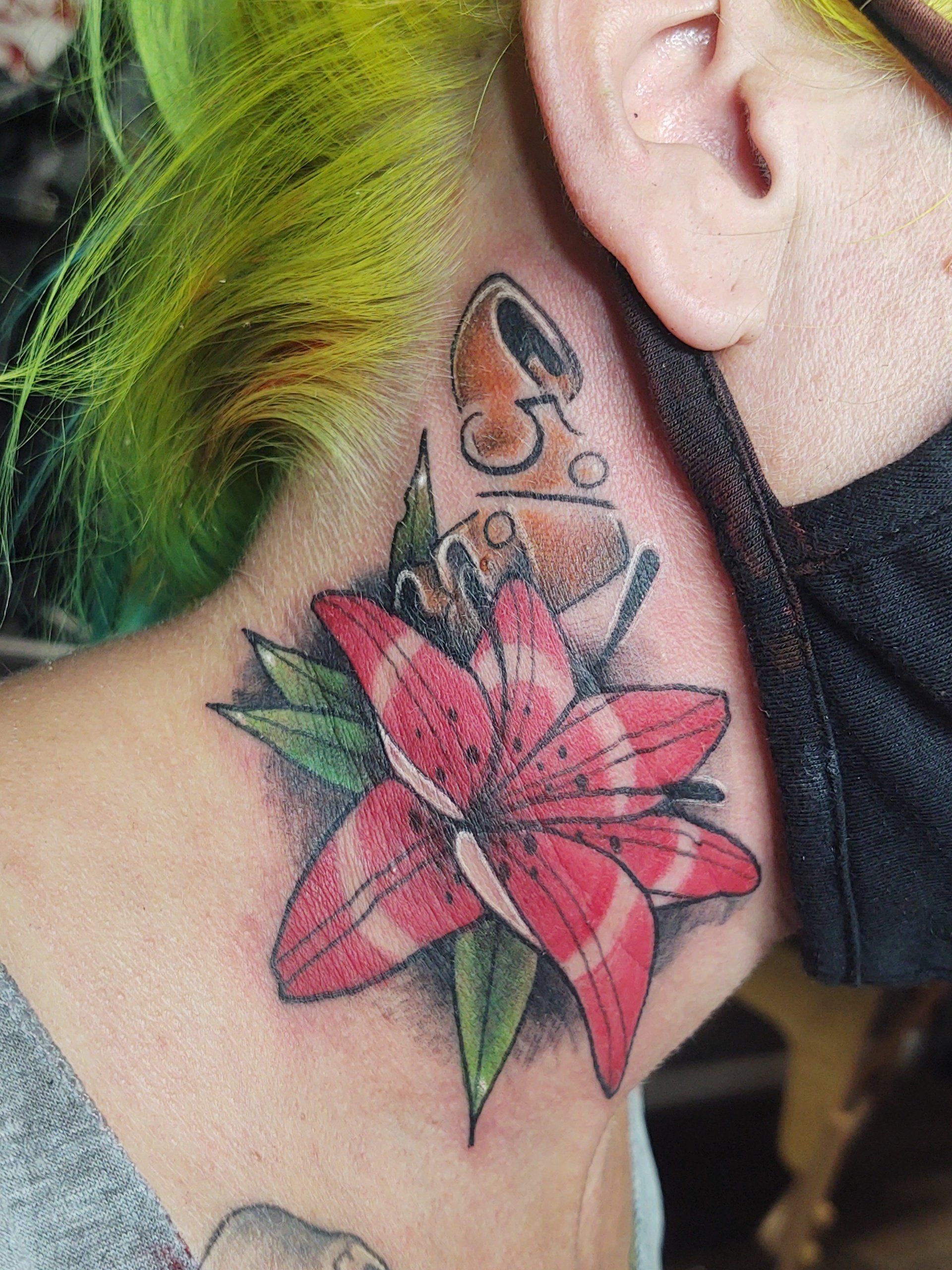 A person with green hair has a tattoo of a flower on their neck