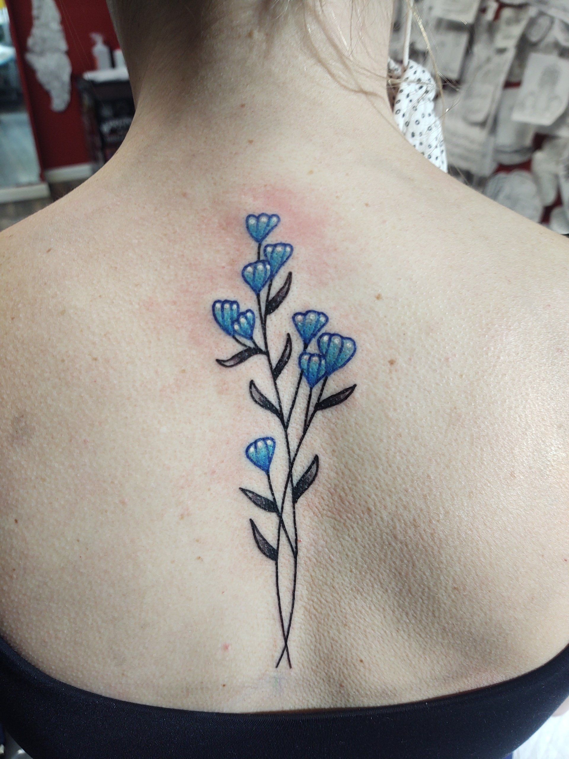 A woman has a tattoo of blue flowers on her back