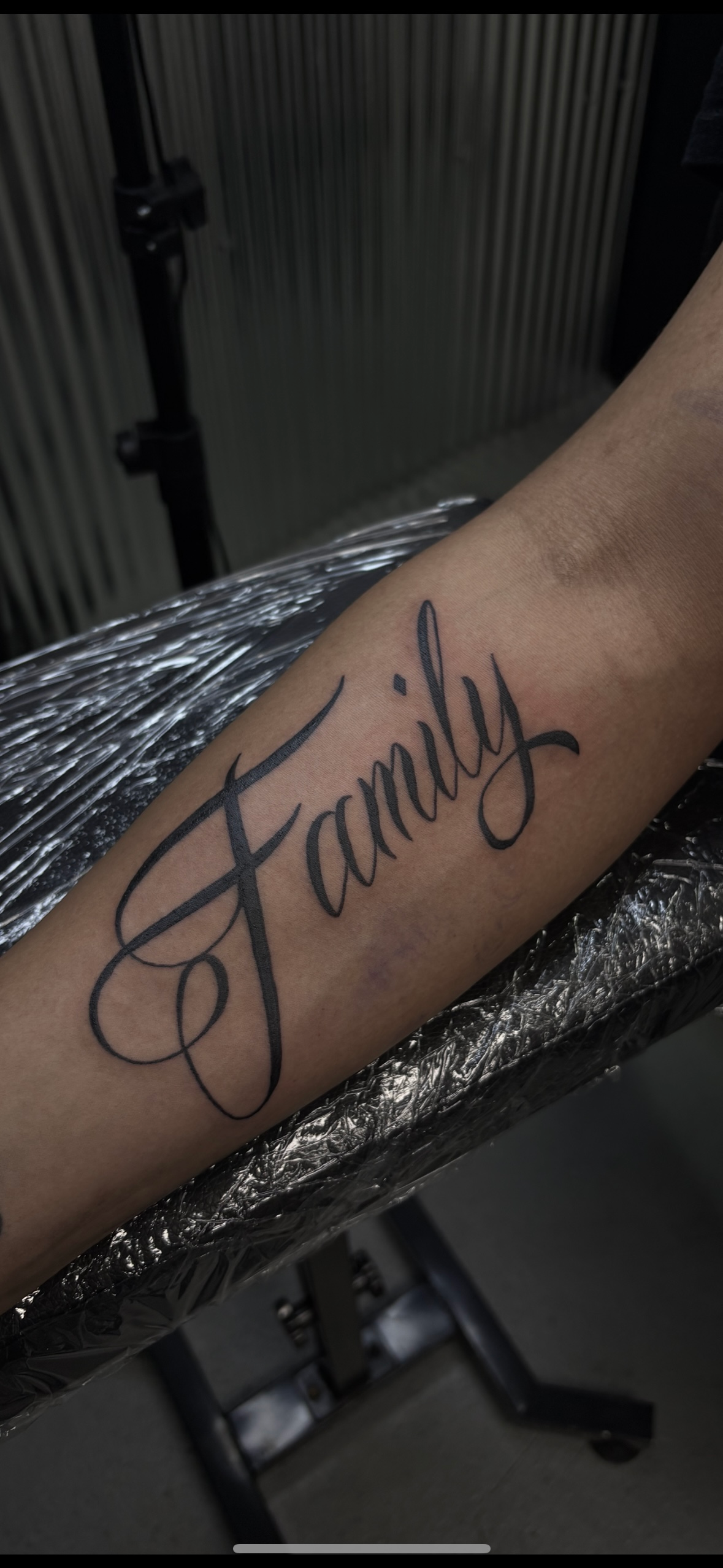 A person has a tattoo of the word family on their forearm.