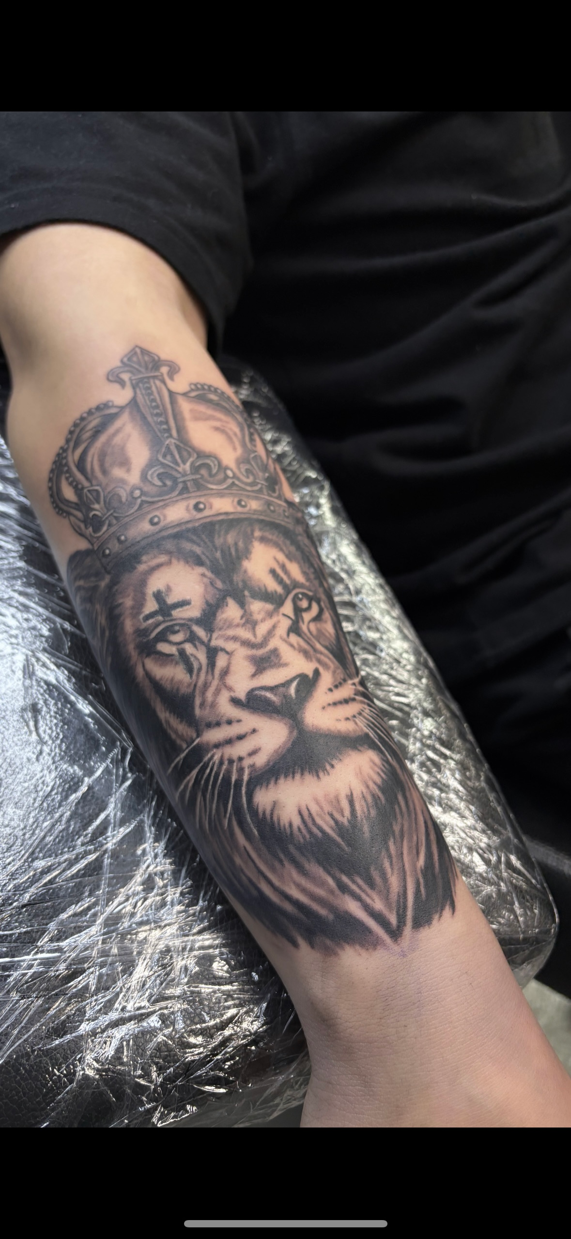 A man has a tattoo of a lion with a crown on his forearm.