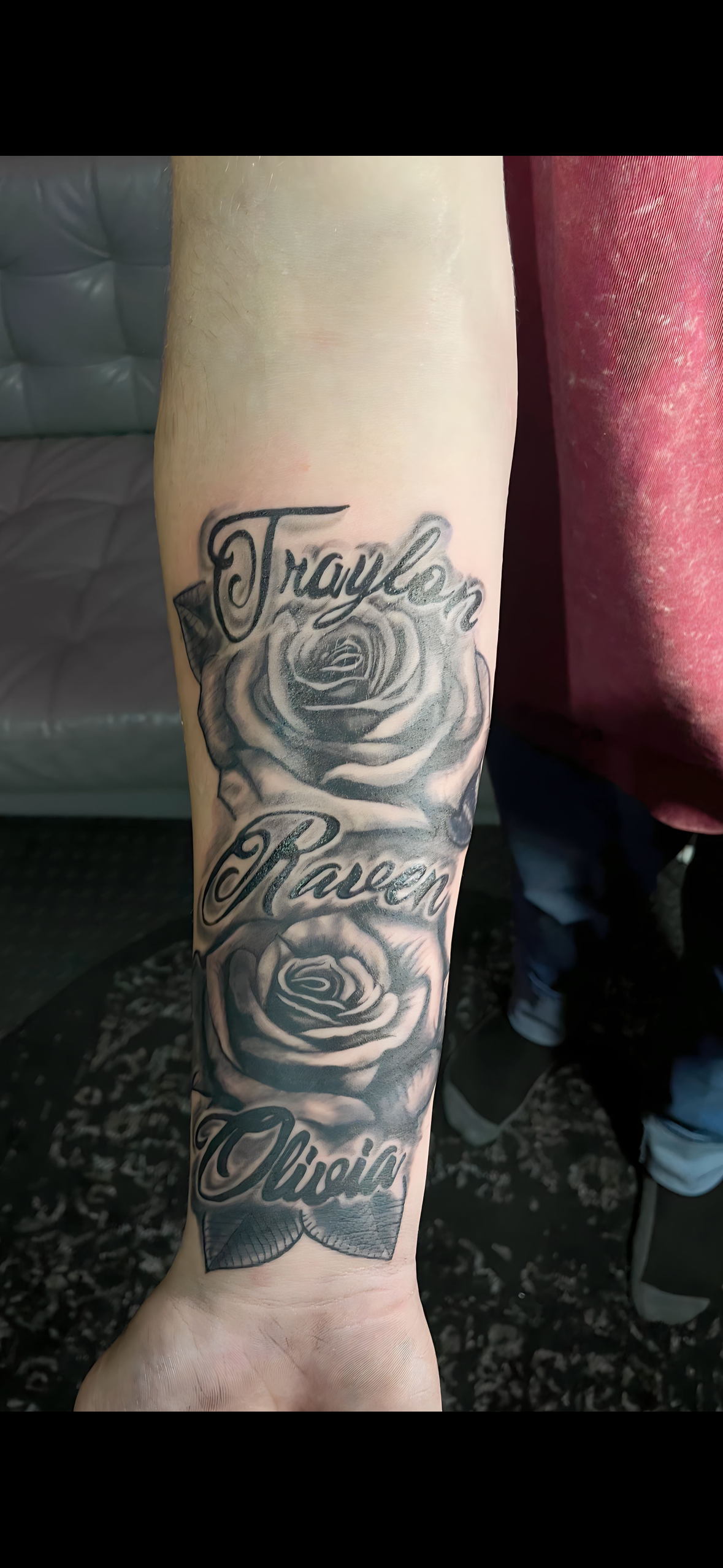 A person has a tattoo on their forearm with roses and the name taylor.