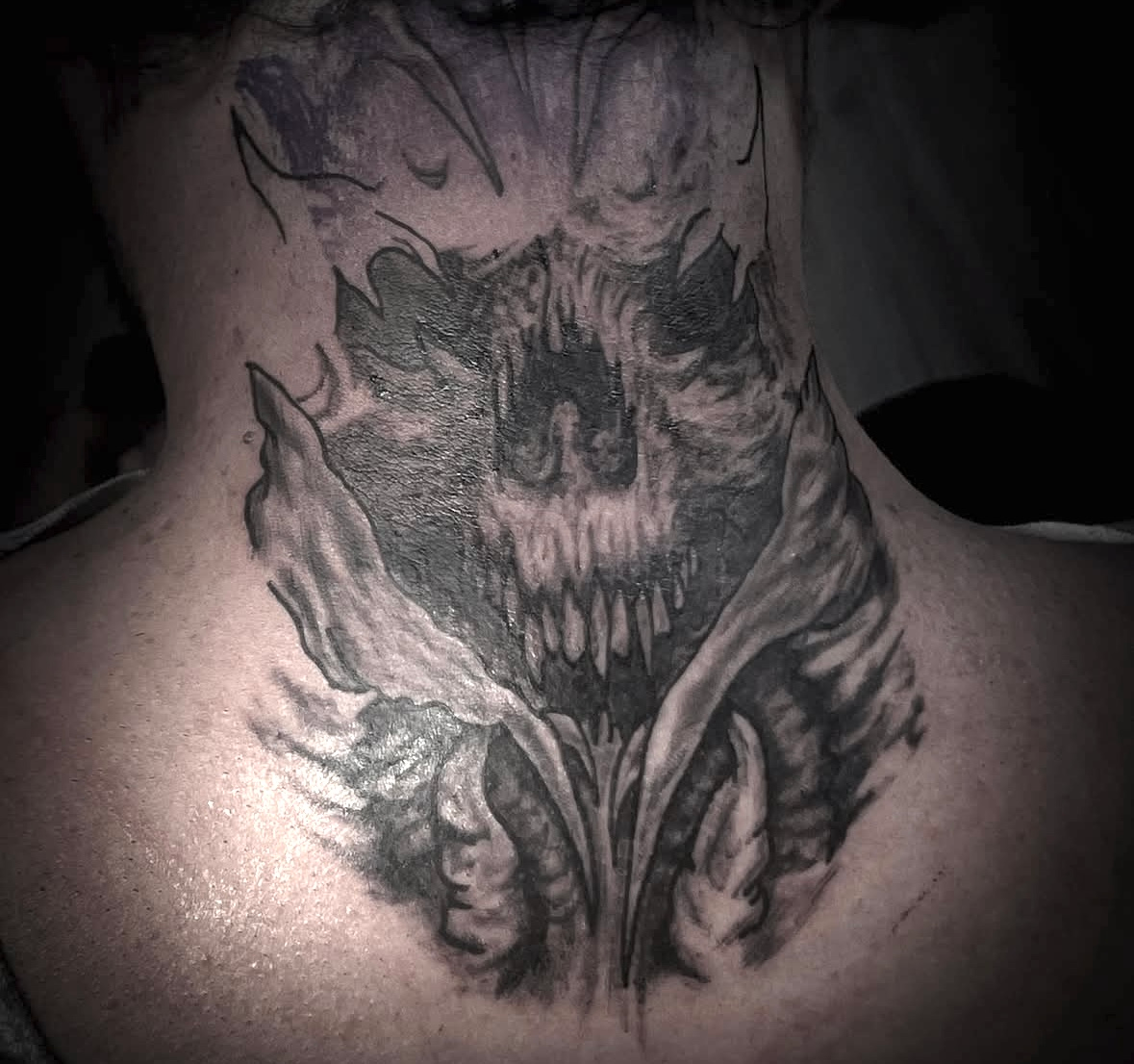 A black and white tattoo on the back of a person 's neck.