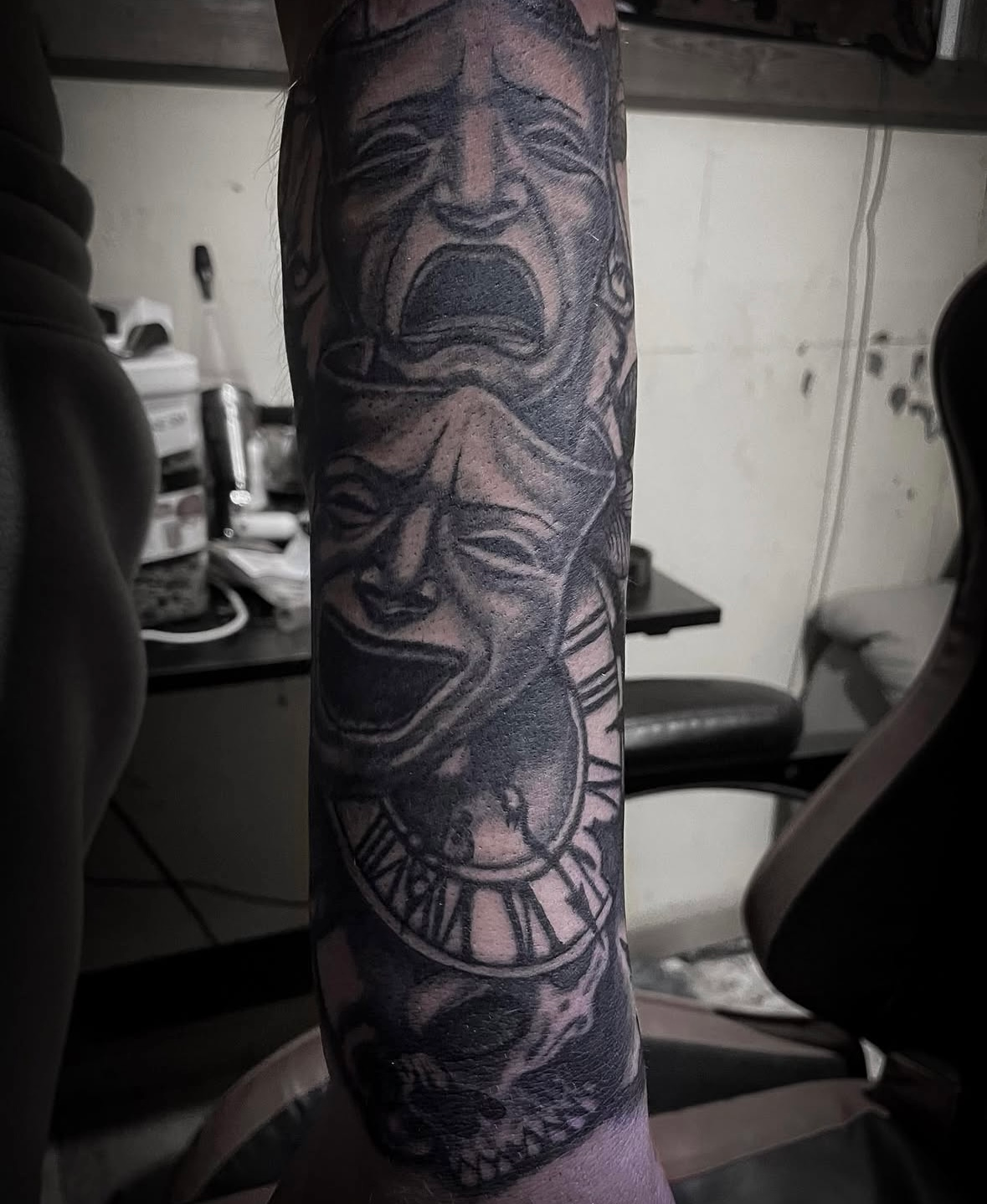 A man has a tattoo of a face and a clock on his arm