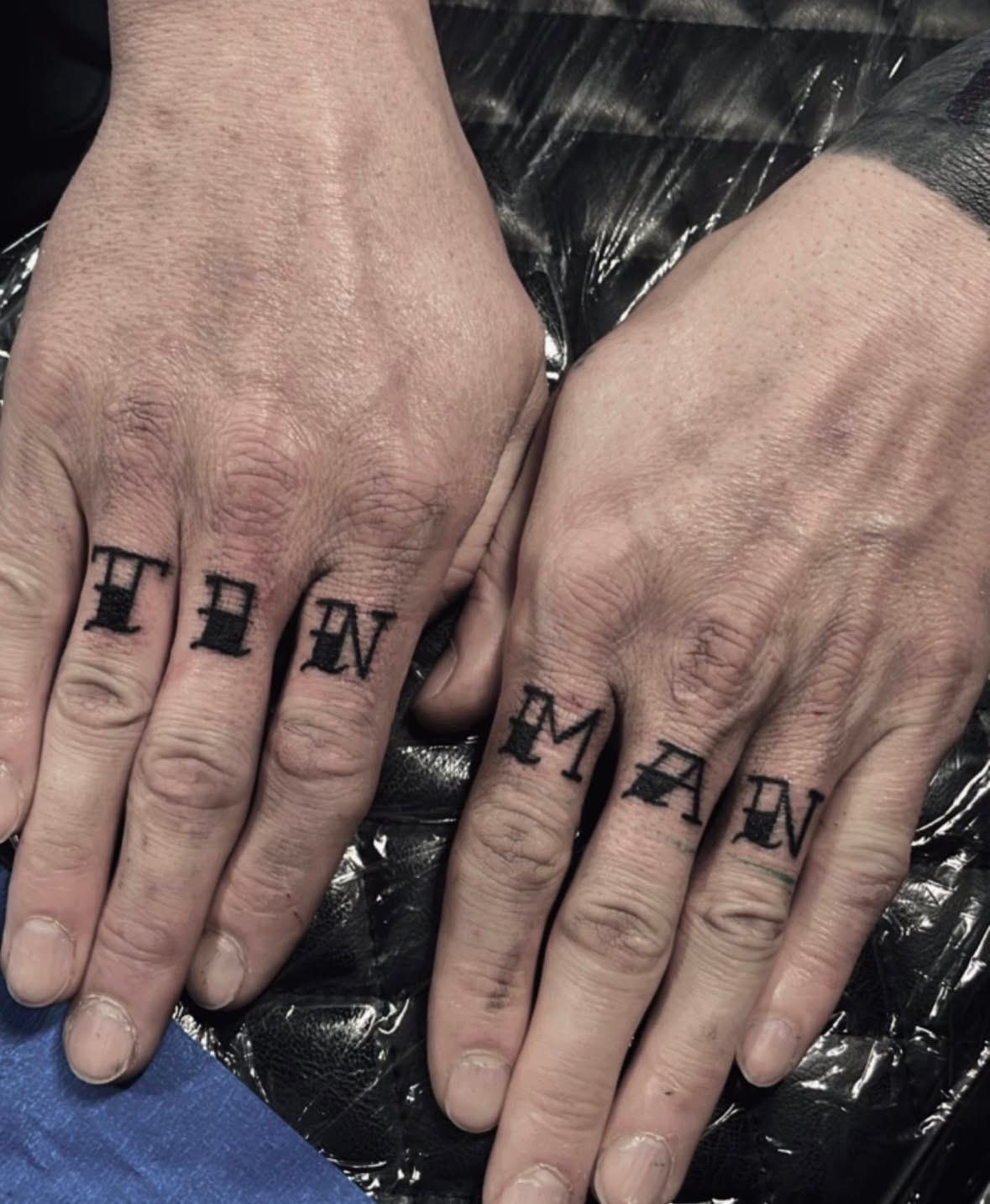 A person has a tattoo on their fingers that says thin man