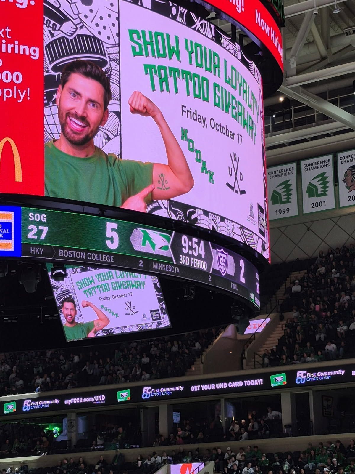 Large screen showing a man flexing an arm, promoting a tattoo giveaway at a hockey game.