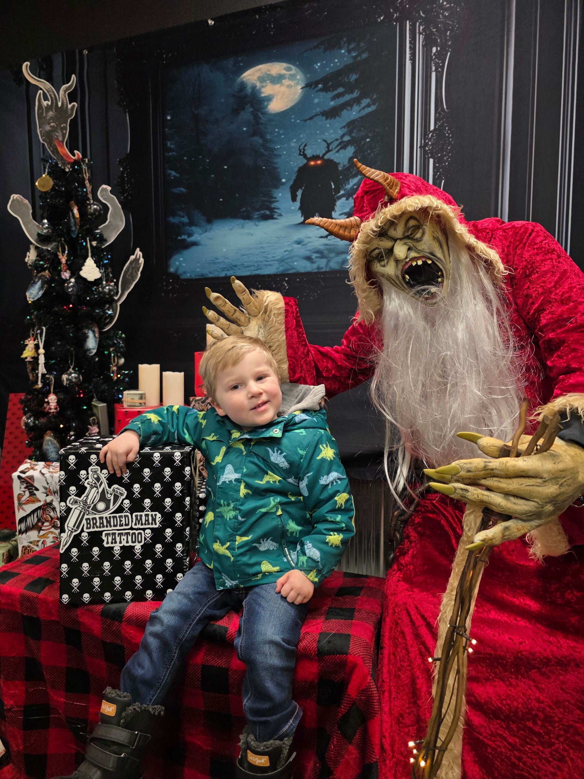 Boy with monster Santa in a decorated room; boy smiles, Santa's reaching out, backdrop has forest/creature.