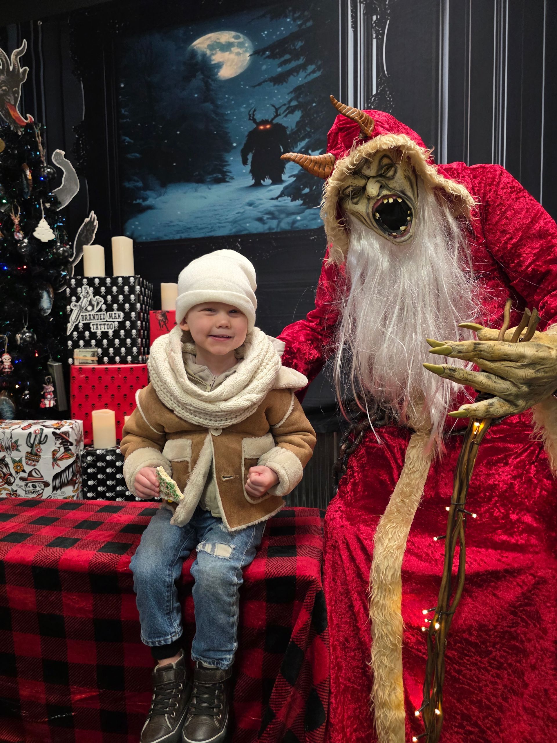Child in winter wear smiles next to a Krampus-like Santa in a festive setting.