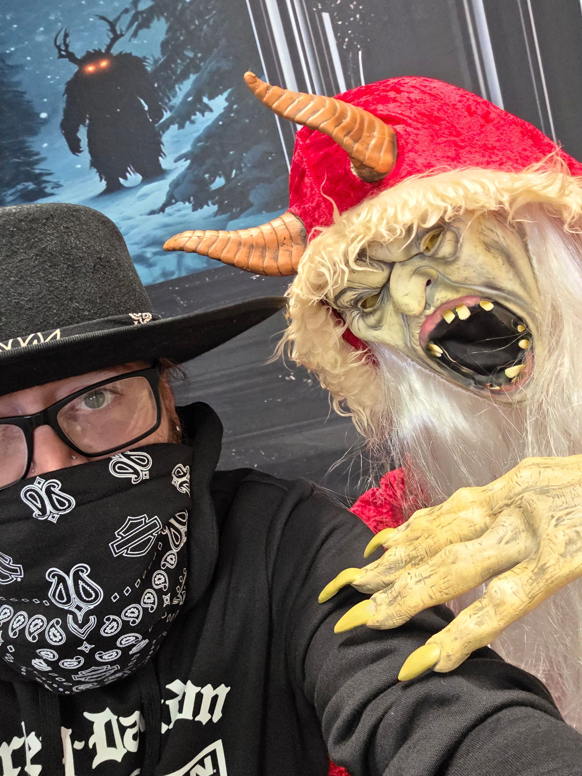 Person in hat and bandana poses with Krampus figure; snowy background, creature silhouette.