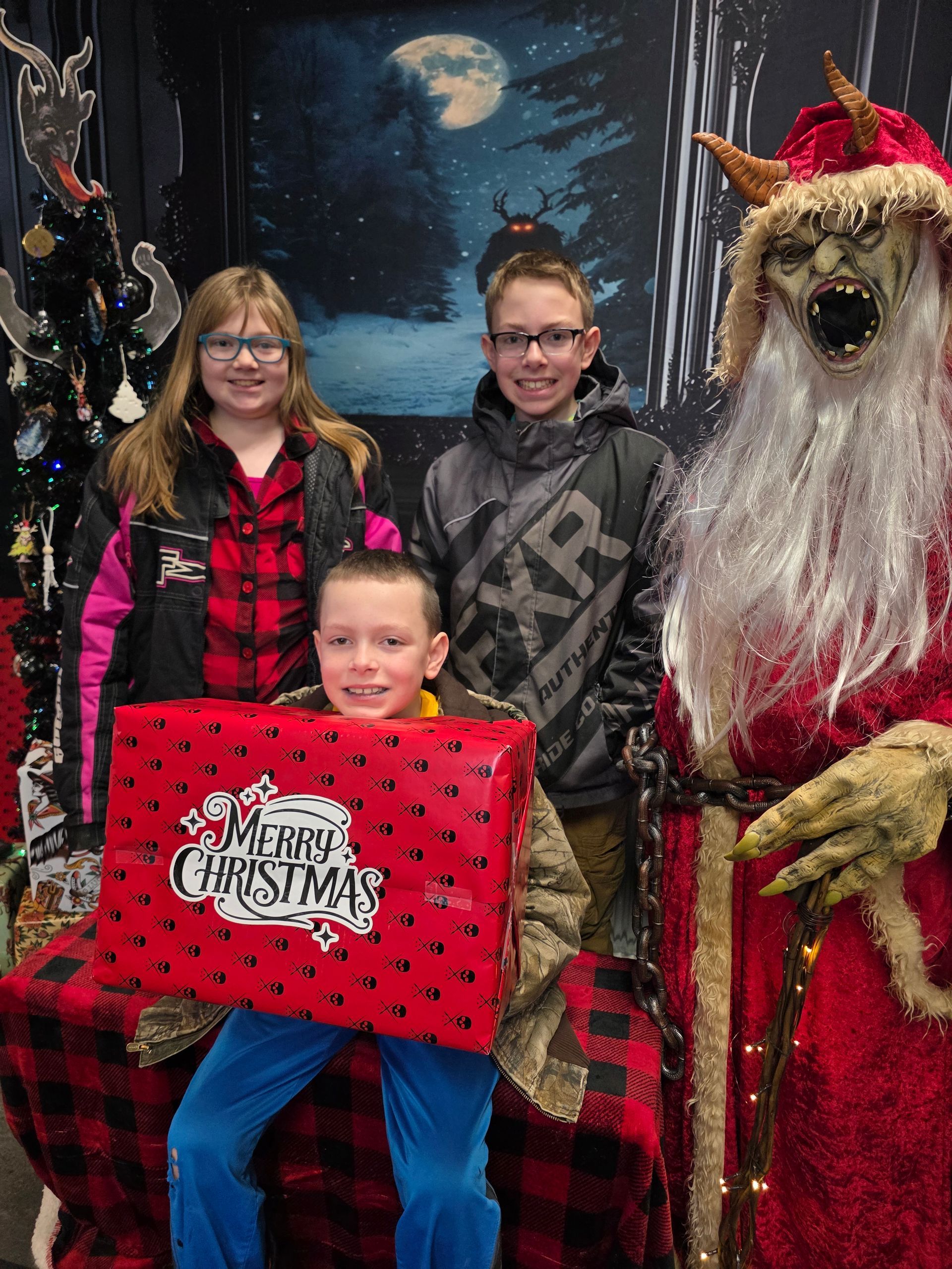 Three children pose with a Krampus-like Santa figure holding a wrapped gift.
