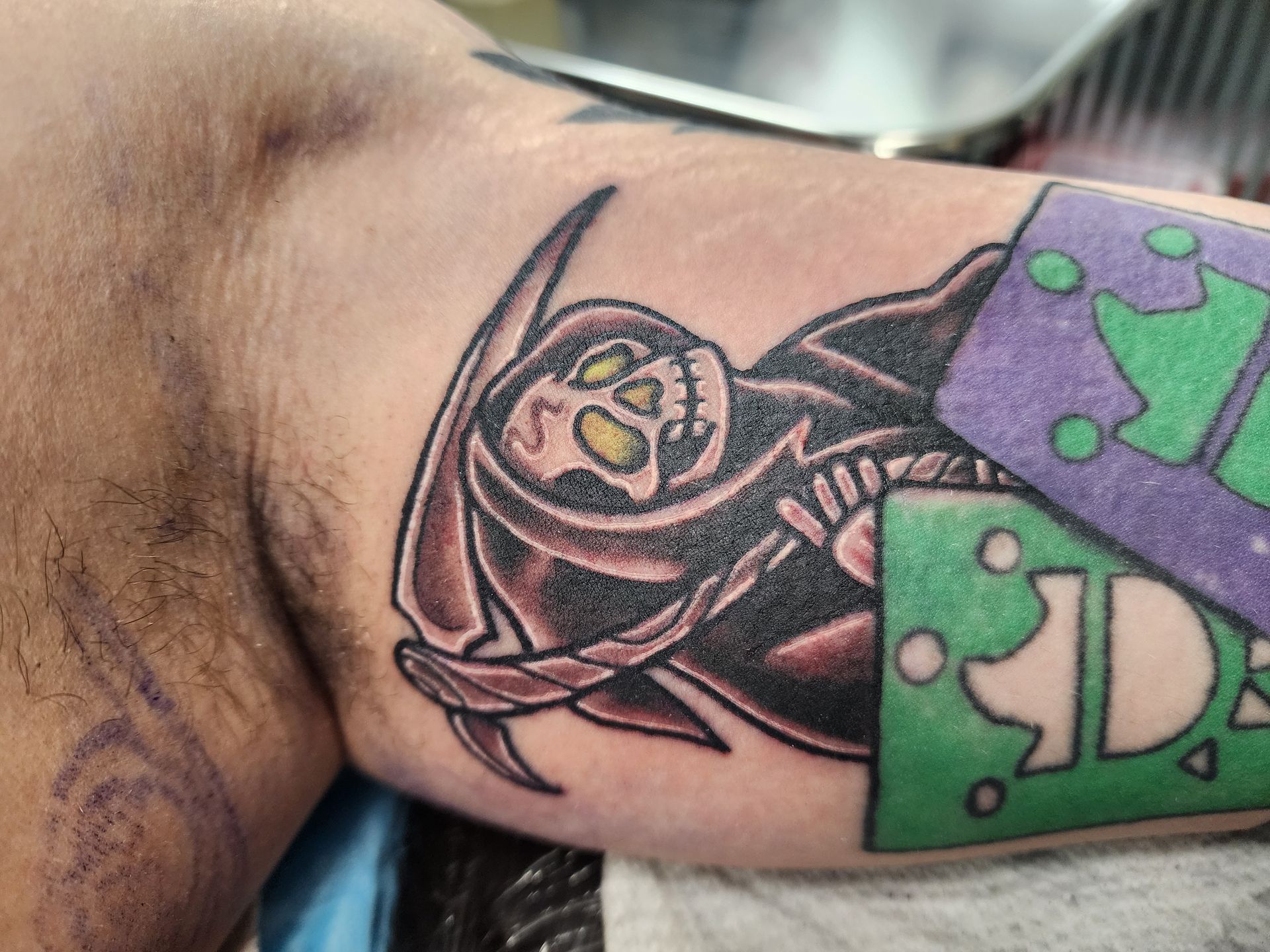 Tattoo of Grim Reaper with a scythe on arm, colorful geometric shapes nearby.