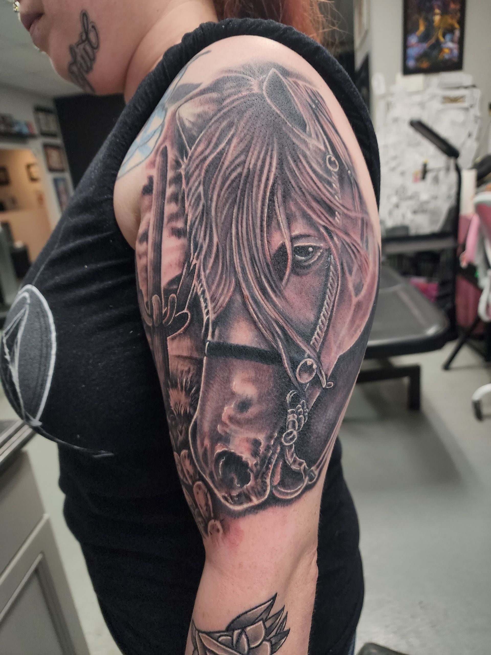 Woman's arm with a detailed black and gray horse tattoo, wearing a bridle, in a studio setting.