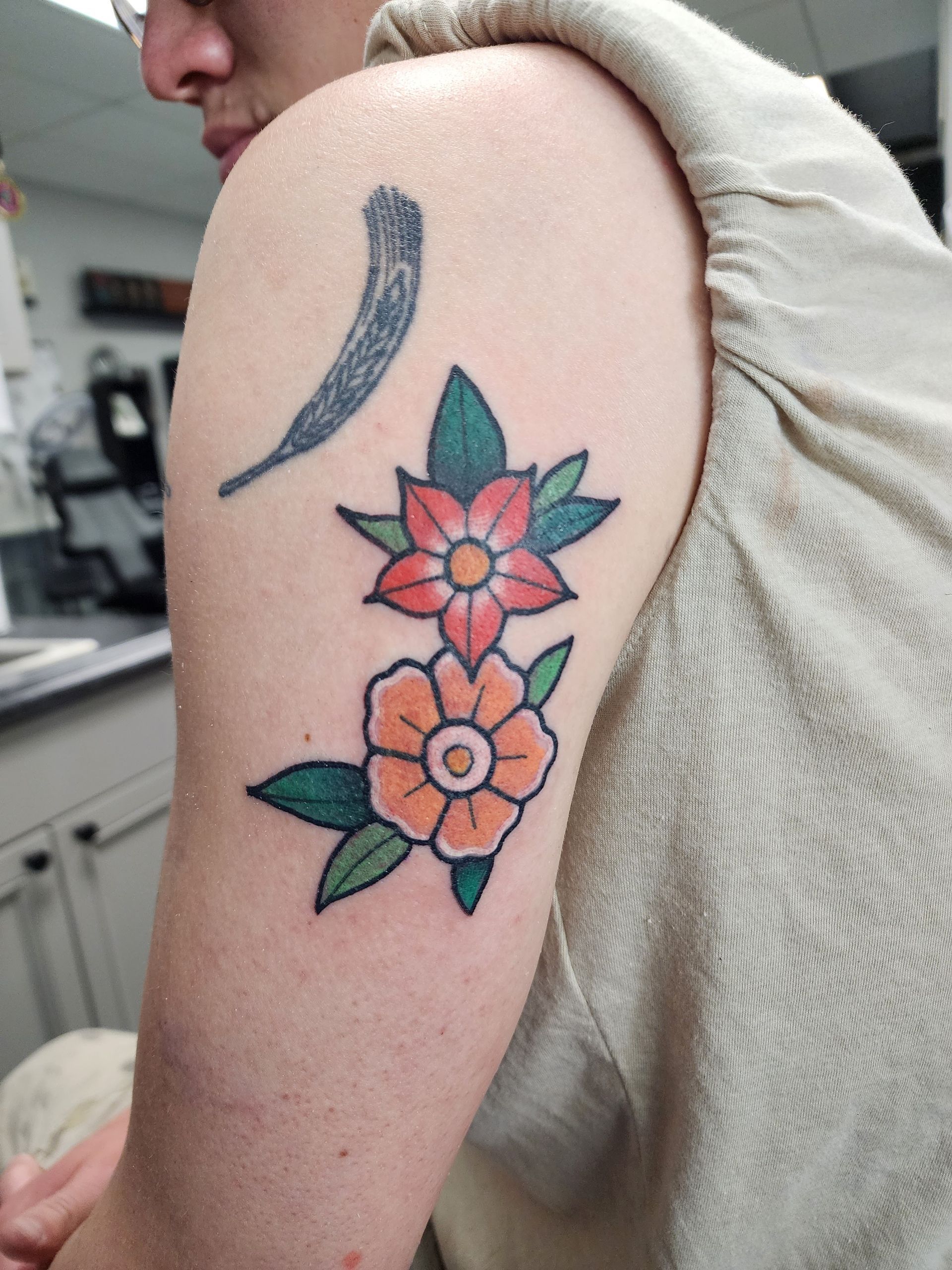 Tattoo of two colorful flowers and a curved shape on a person's upper arm.