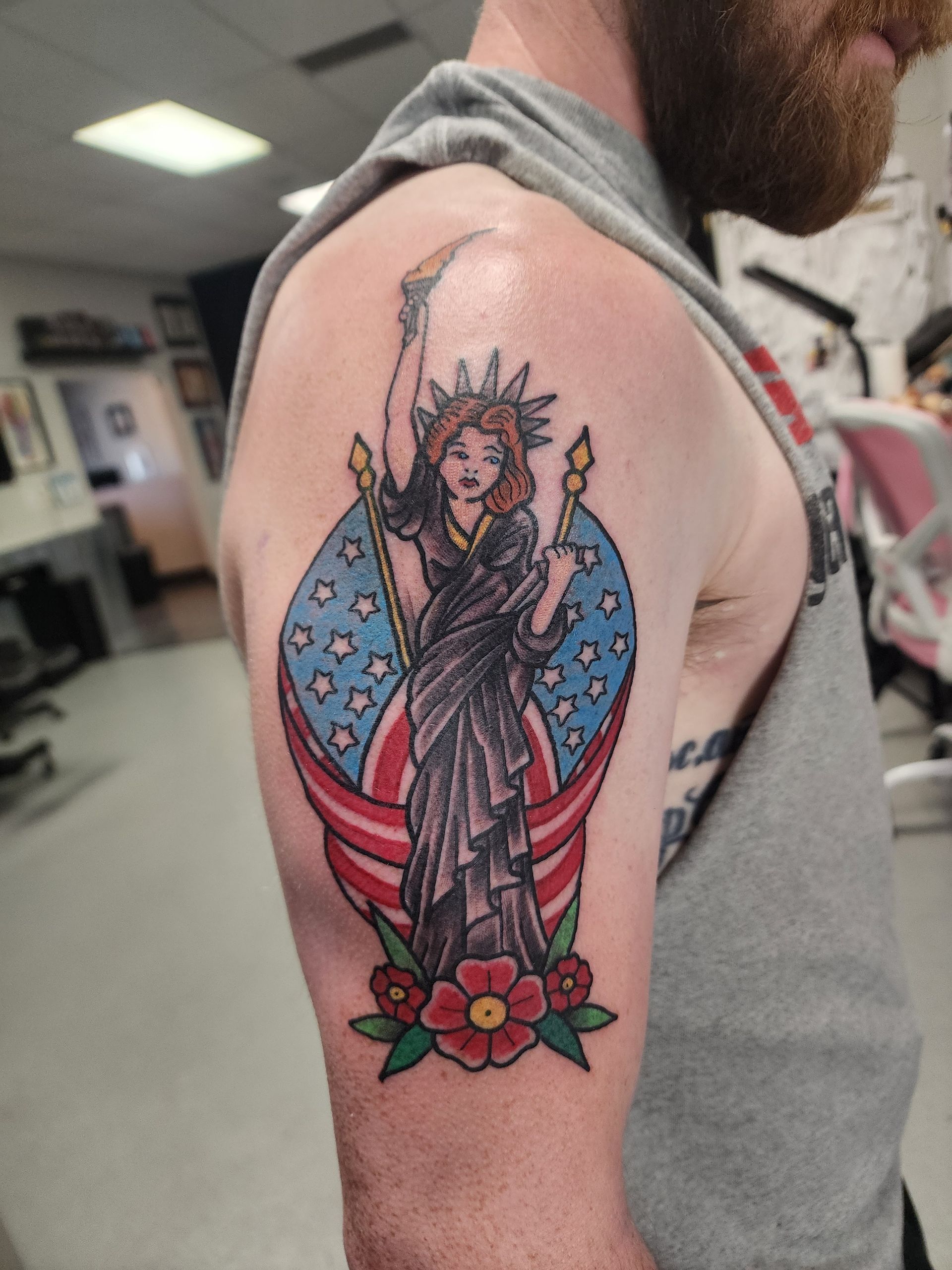 Tattoo of the Statue of Liberty on a person's upper arm. American flag, flowers, and a crescent shape surround the statue.