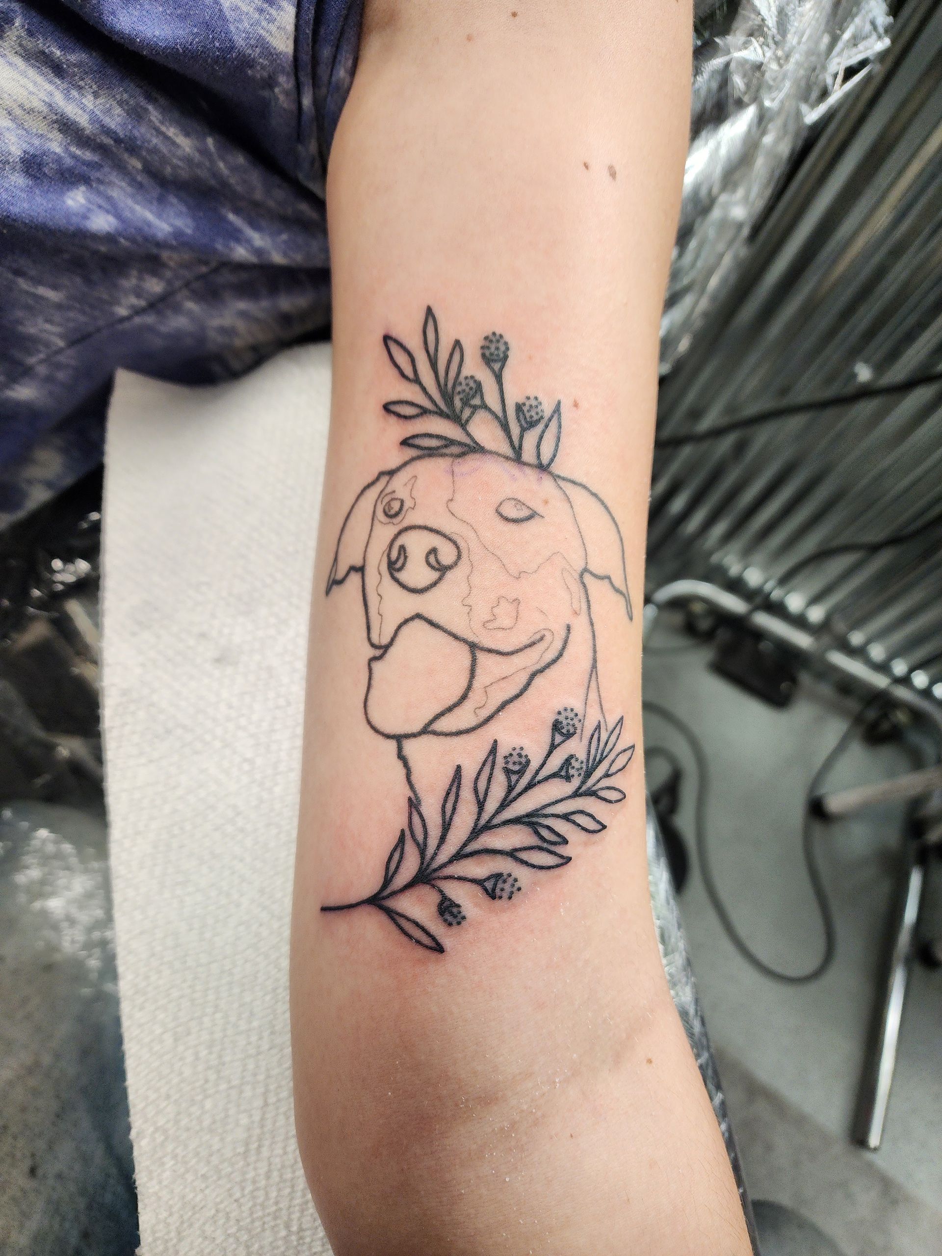 Line art tattoo of a dog with flowers on a forearm.