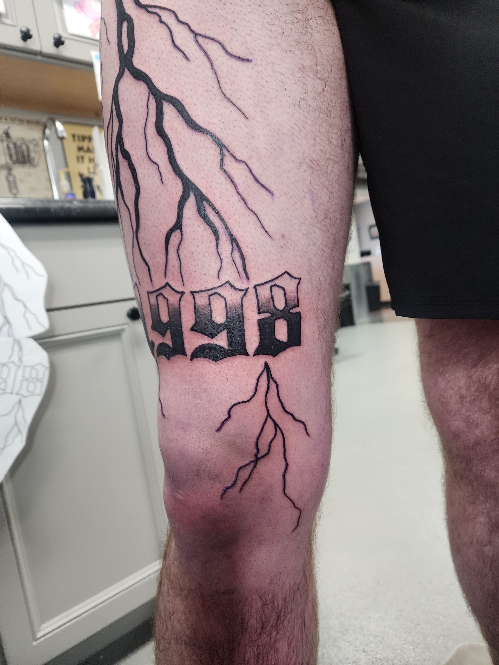 Leg tattoo with the numbers 998 and lightning bolts.