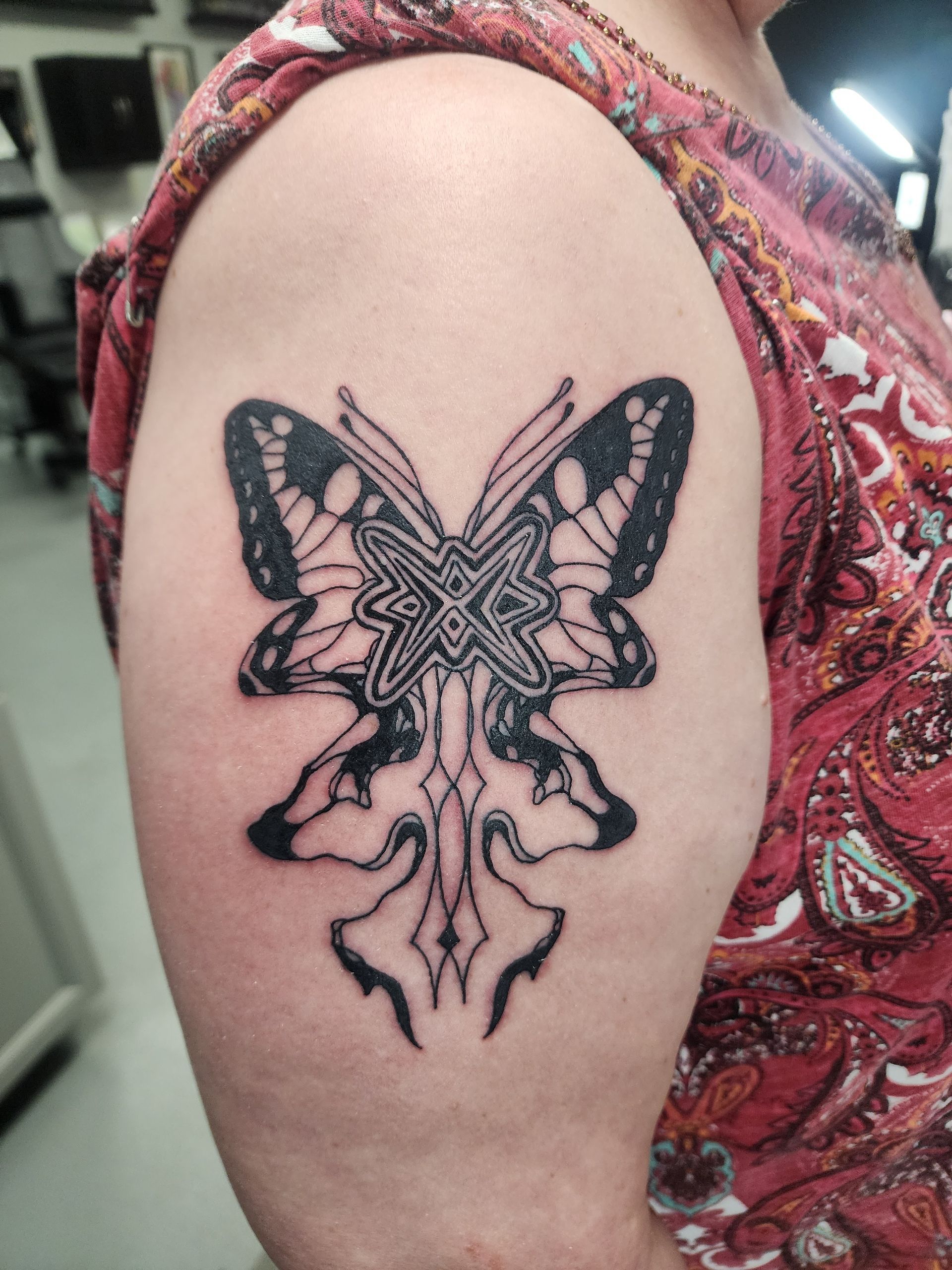 Tattoo of a black butterfly on a person's upper arm, with an ornate design and detailed wings.