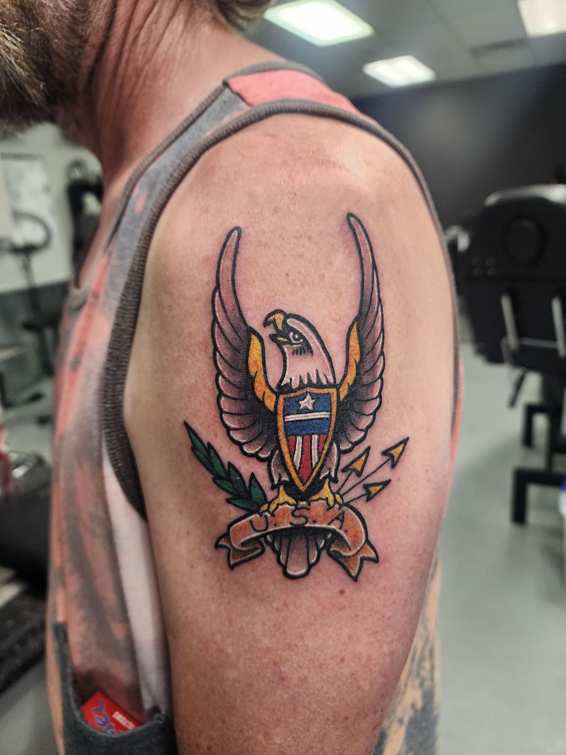 Tattoo of an eagle with outstretched wings and a shield on a person's shoulder.