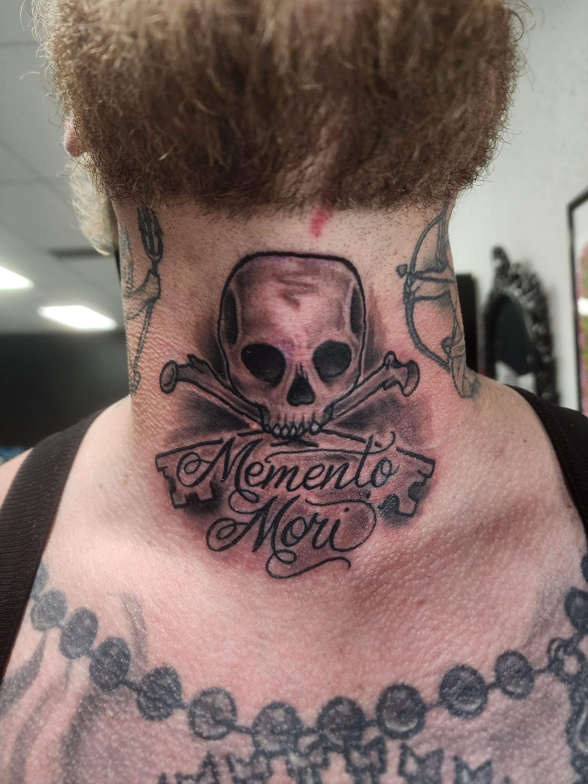 Tattoo on a neck: skull with crossed bones, banner reading
