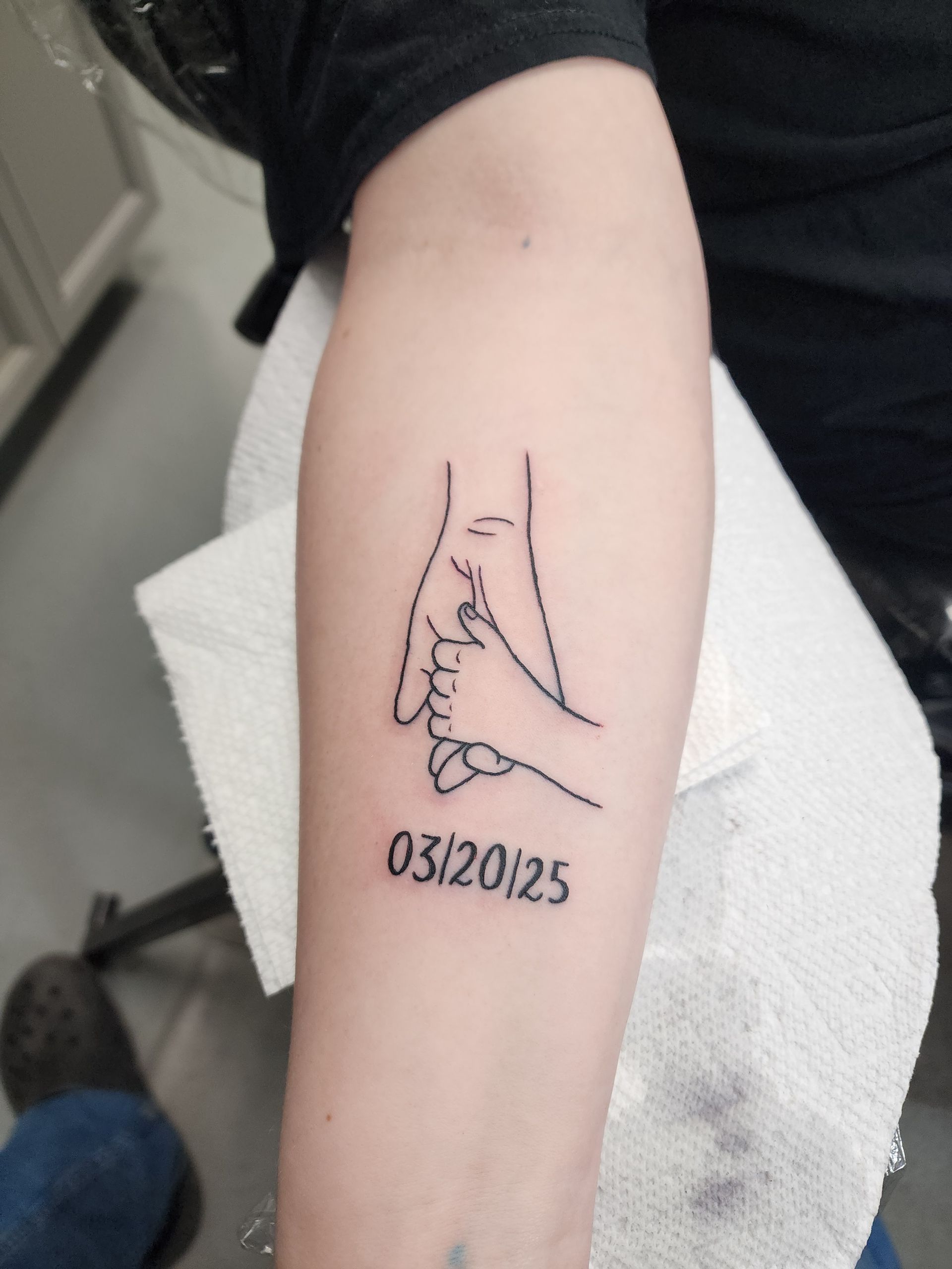 Line art tattoo of an adult and child's hands holding with the date 03/20/25 below.