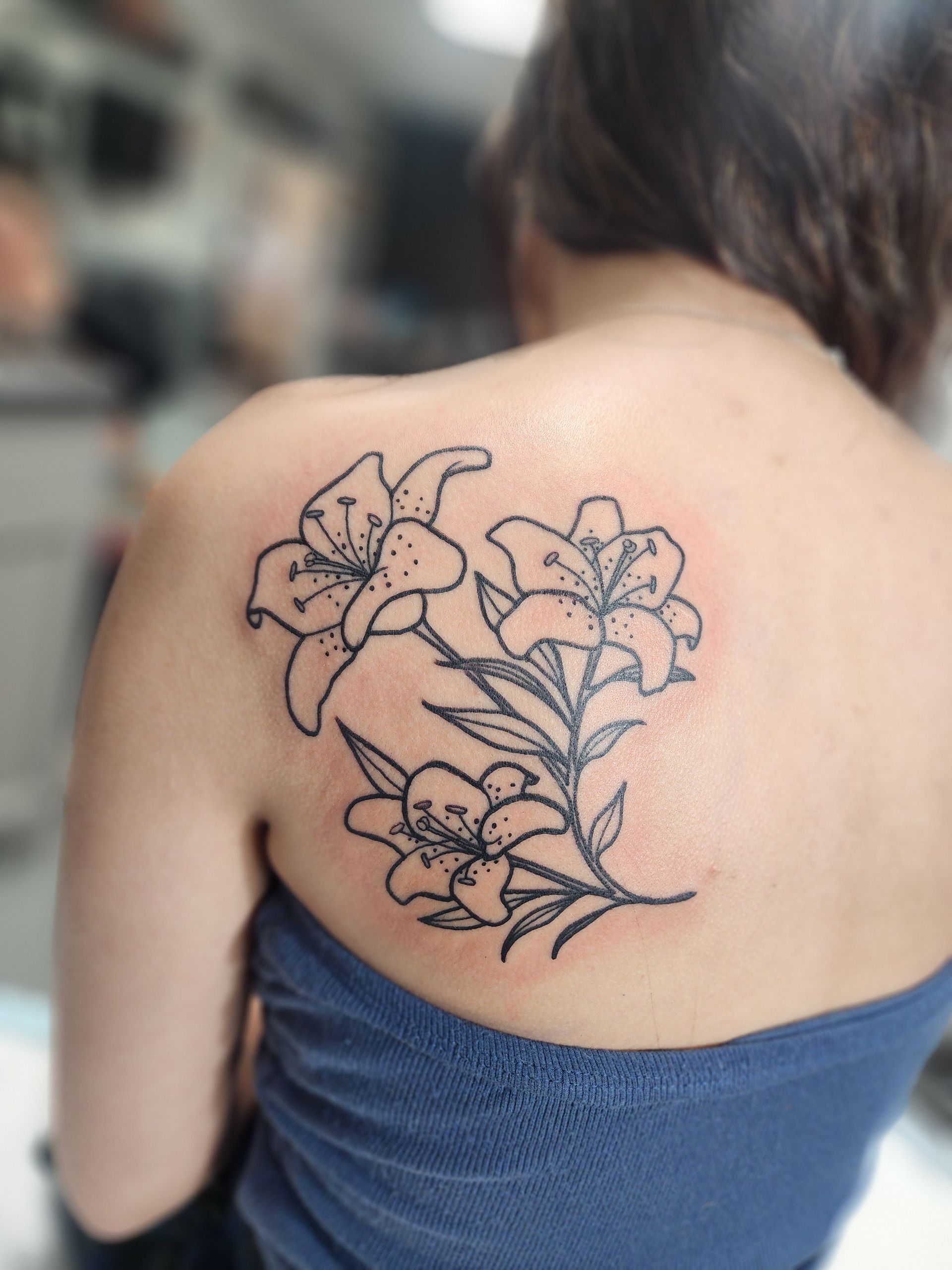 Black outline lily tattoo on a person's upper back and shoulder.