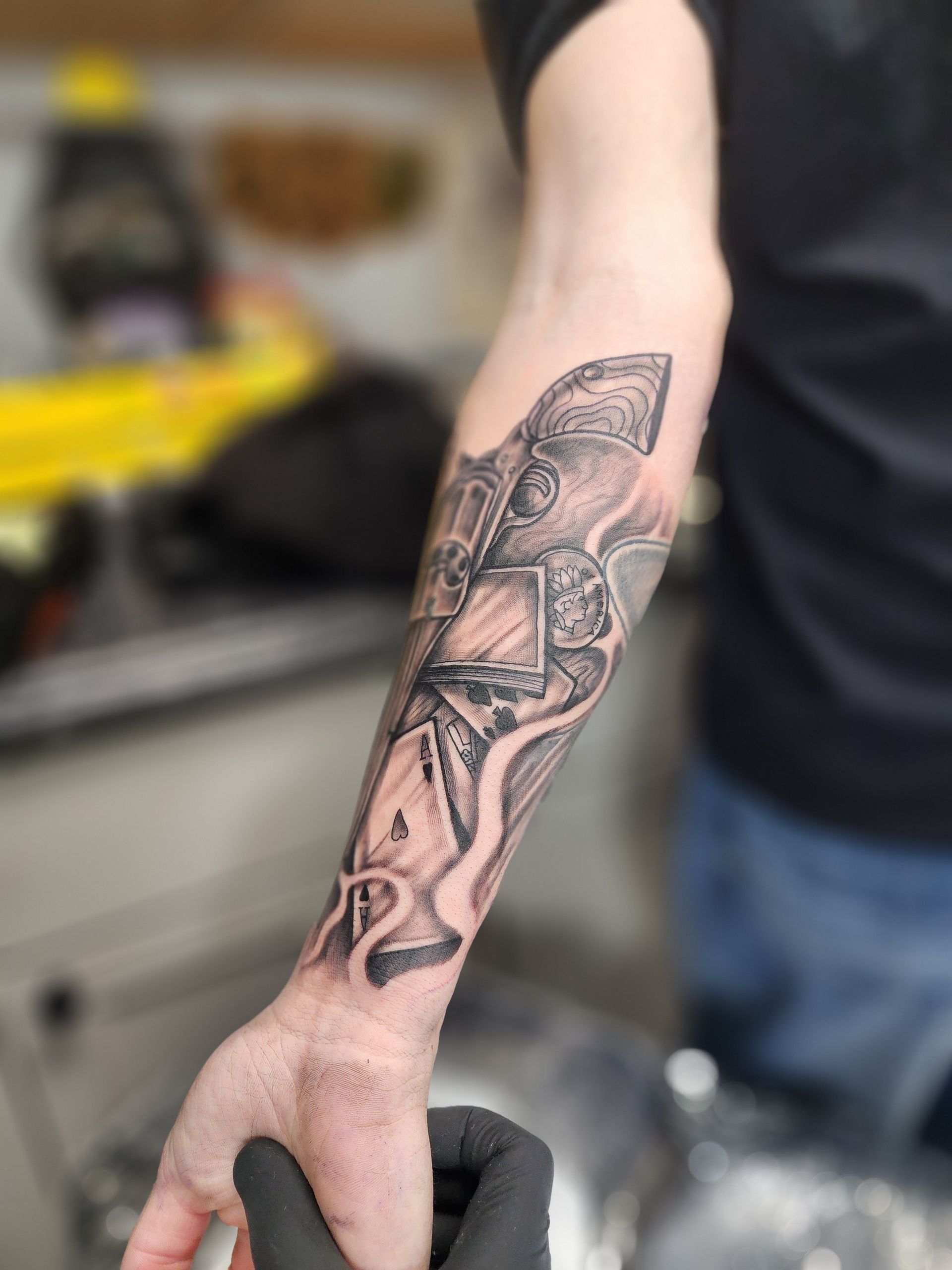 Tattoo on forearm: gears and abstract shapes in black and gray, hand wearing black glove.