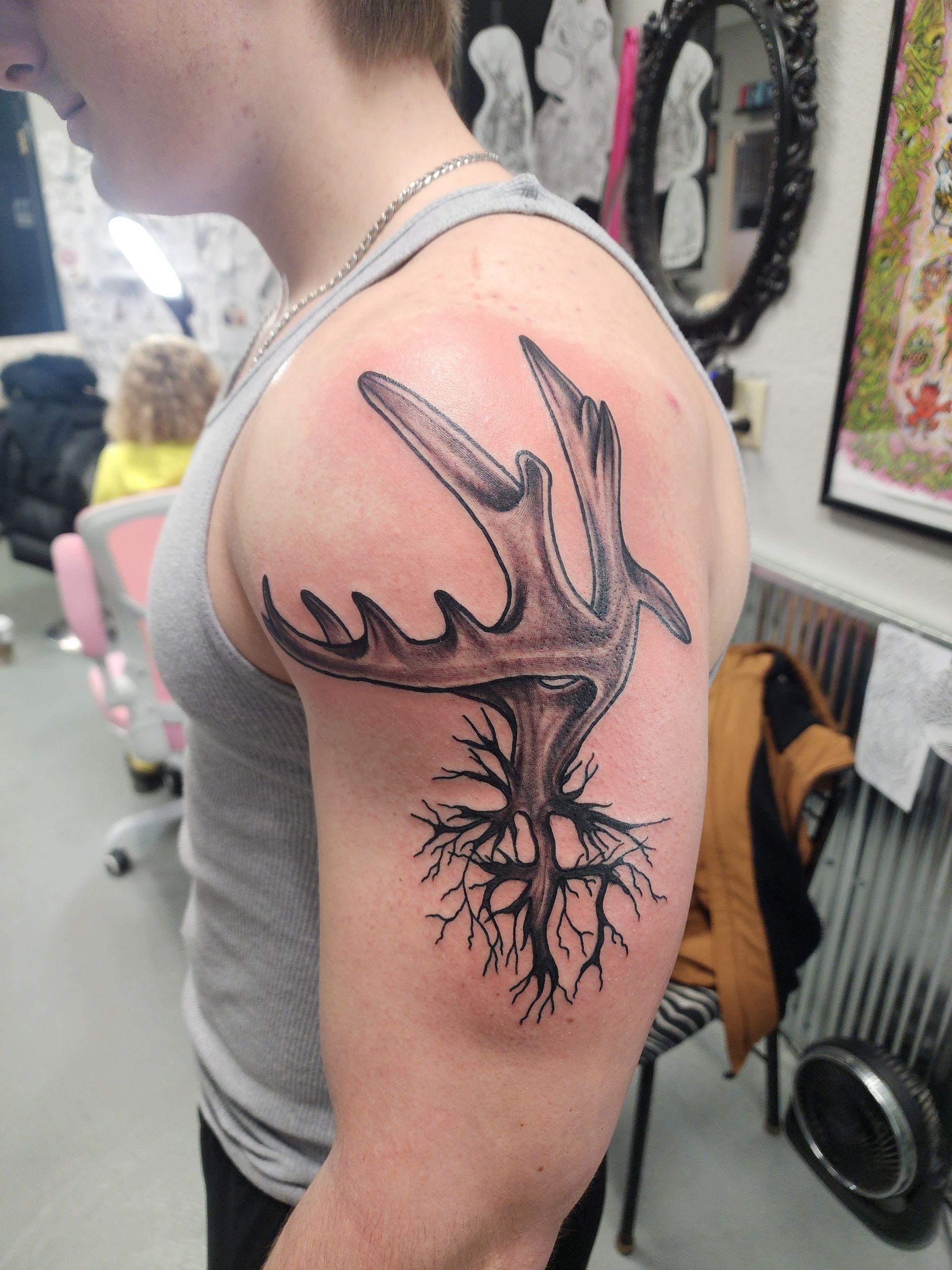 Tattoo of a moose antler sprouting roots on a person's upper arm.