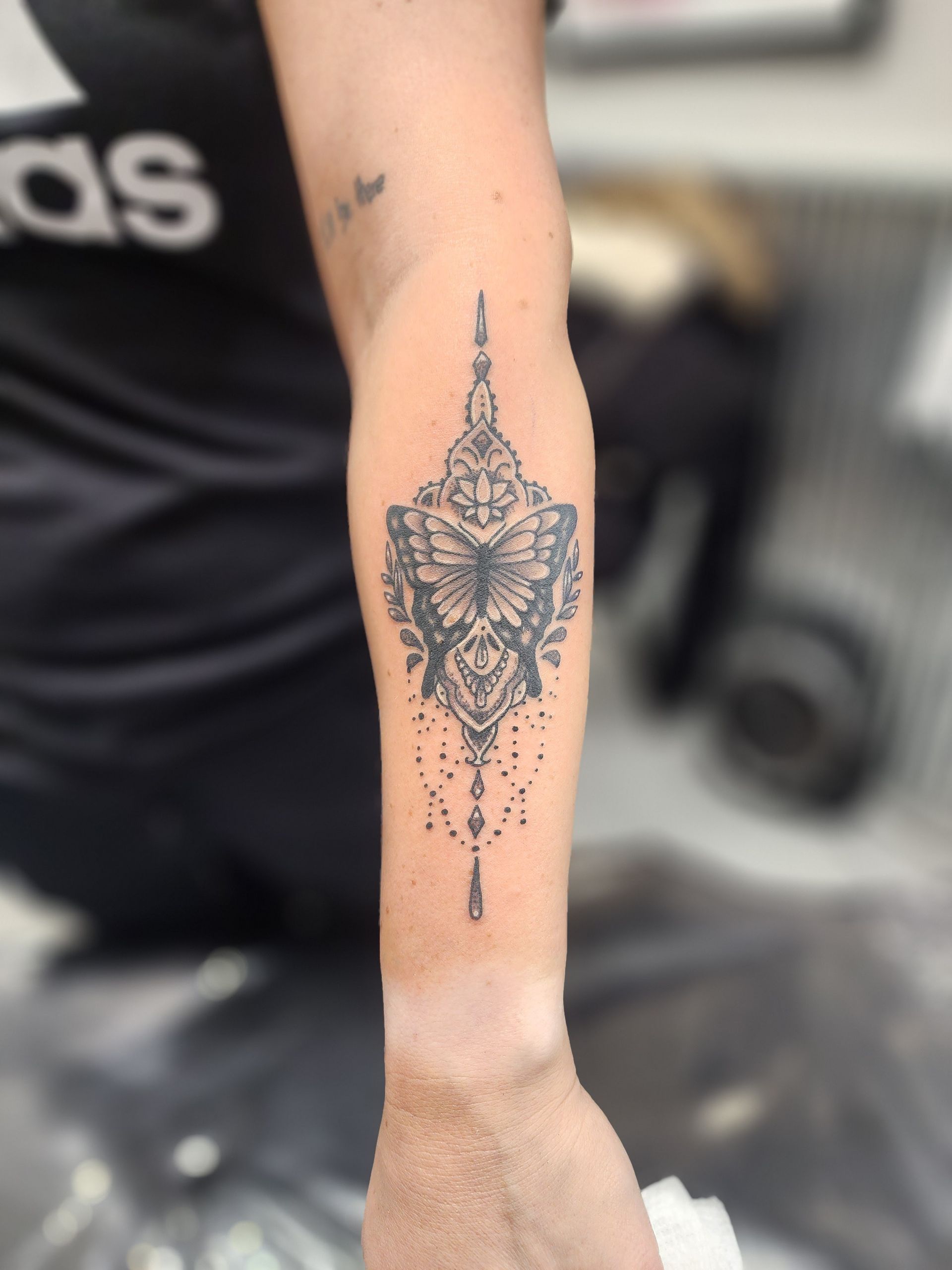 Tattoo of a butterfly inside an ornate, symmetrical design on a forearm.