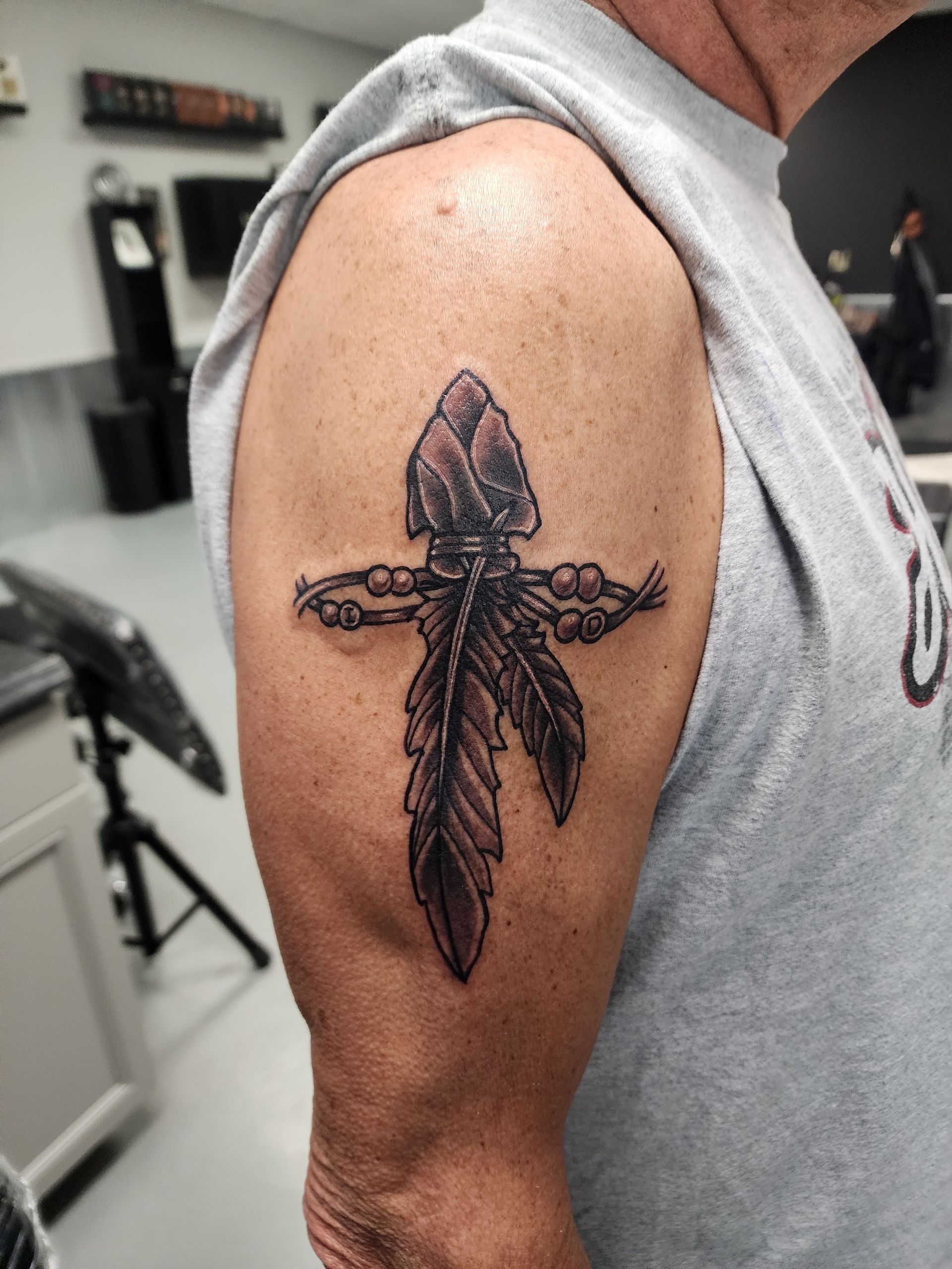 Tattoo of an arrowhead with feathers, on a man's upper arm.