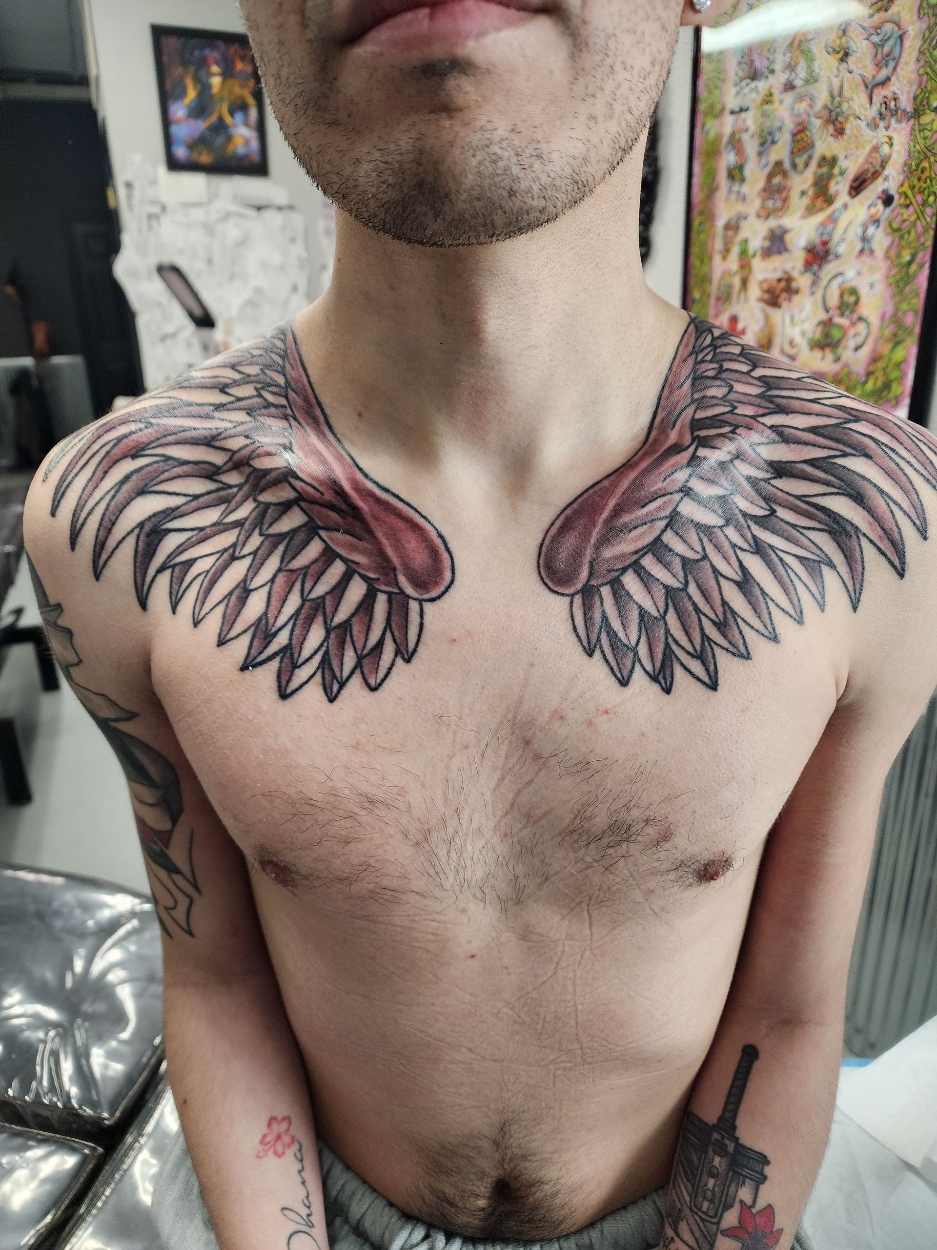 Man with a chest tattoo of angel wings, with red and grey details.