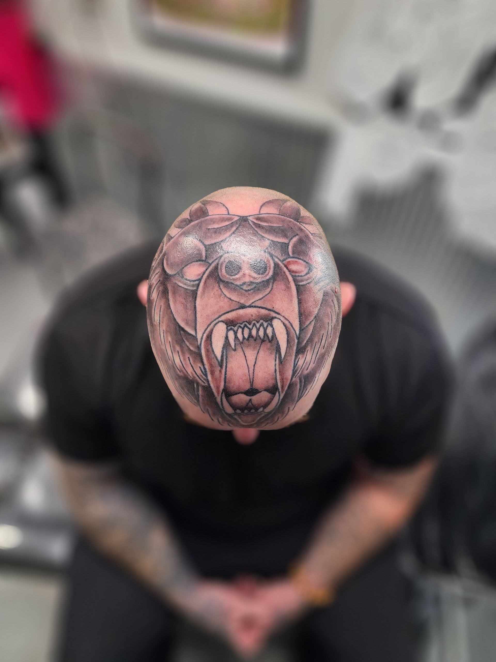 Man with a bald head tattooed with a roaring bear's head. Viewed from above, with blurry background.