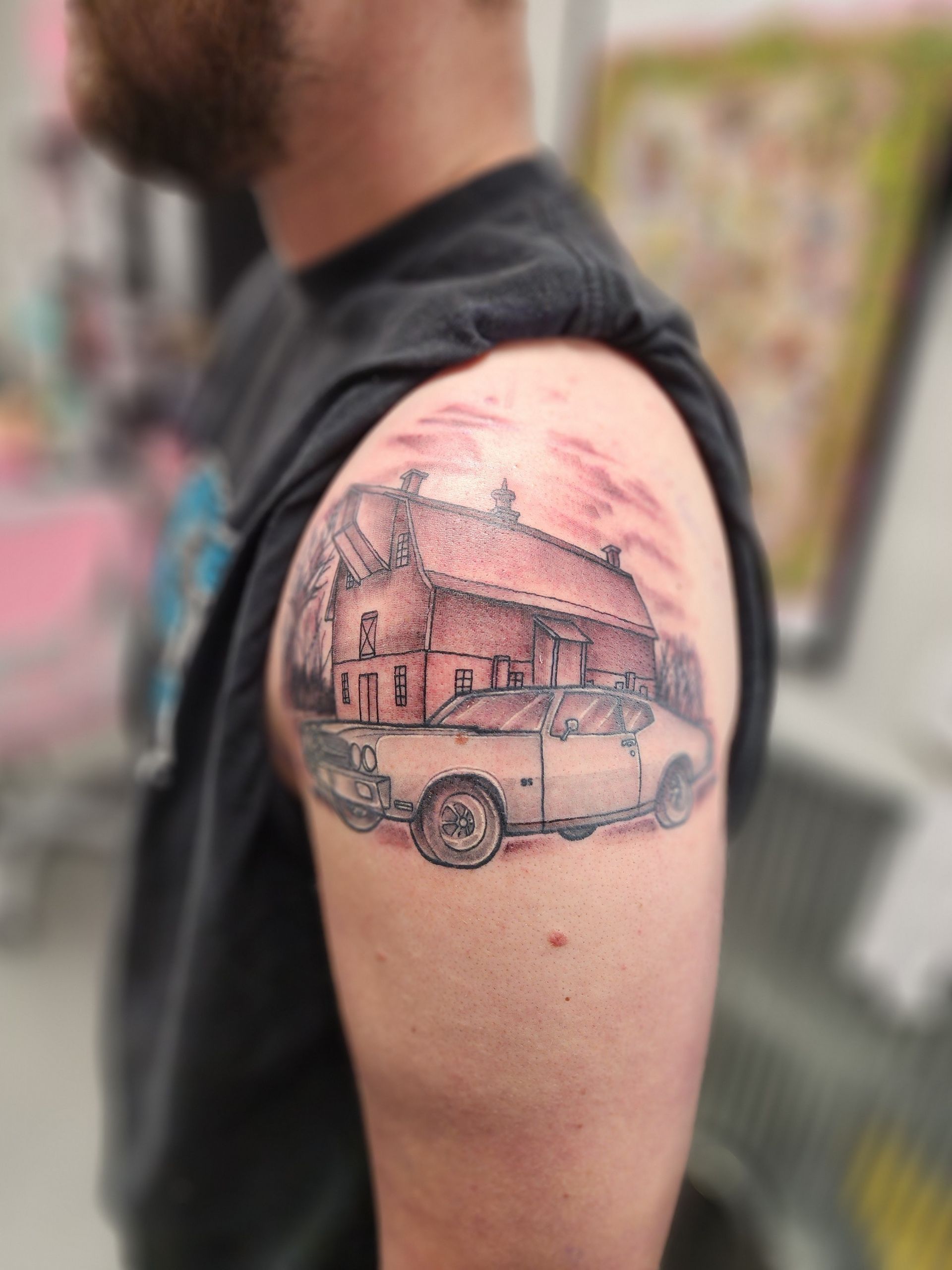 Tattoo on a person's shoulder, featuring a car and building under a pink sky.